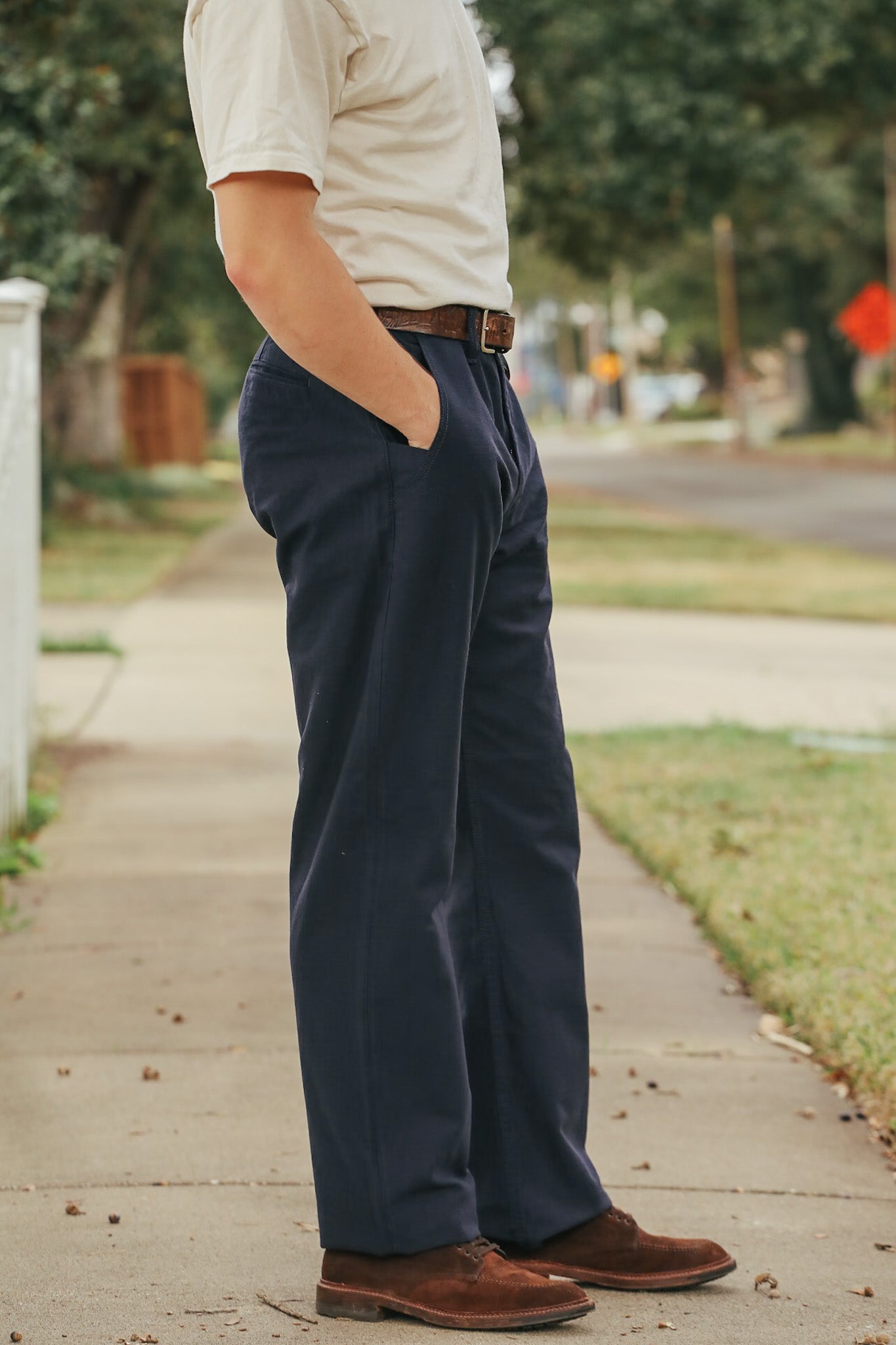 Person wearing navy pants and brown shoes on a sidewalk with a blurred background