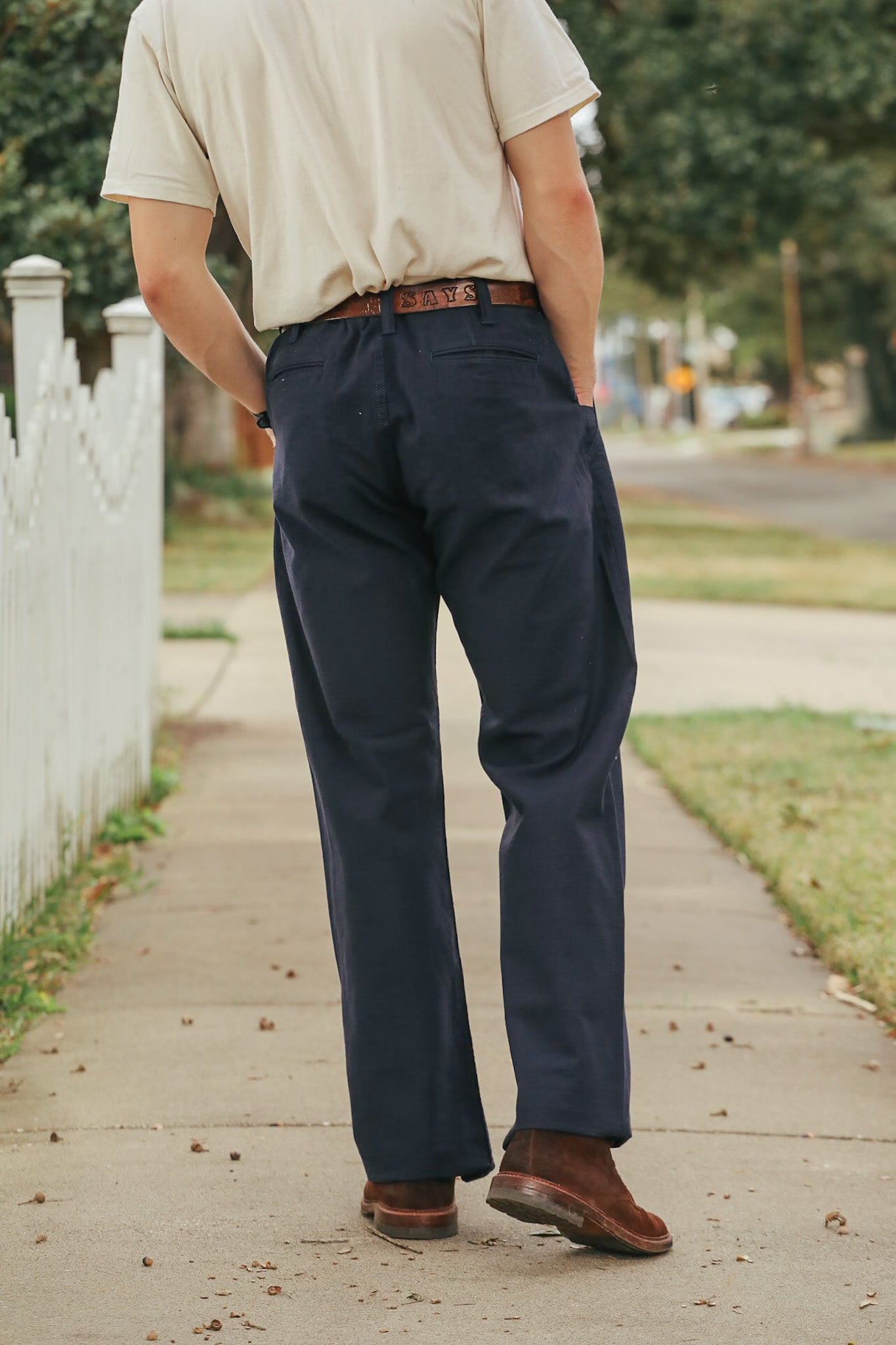 Person wearing navy pants and a beige shirt walking on a sidewalk.