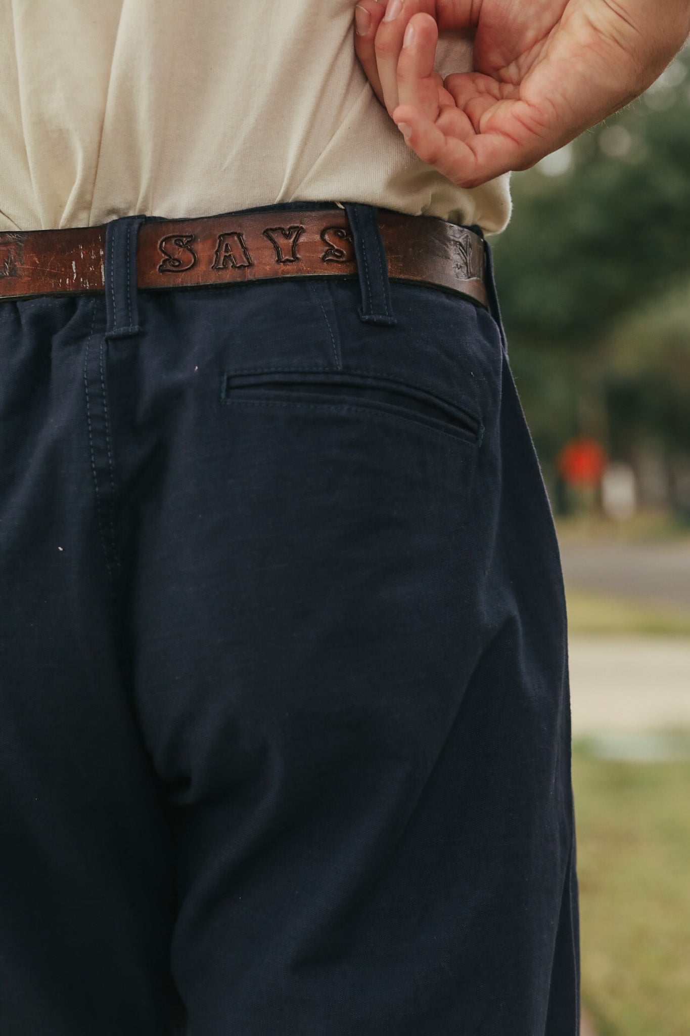 Person wearing navy pants with a brown belt and visible text.