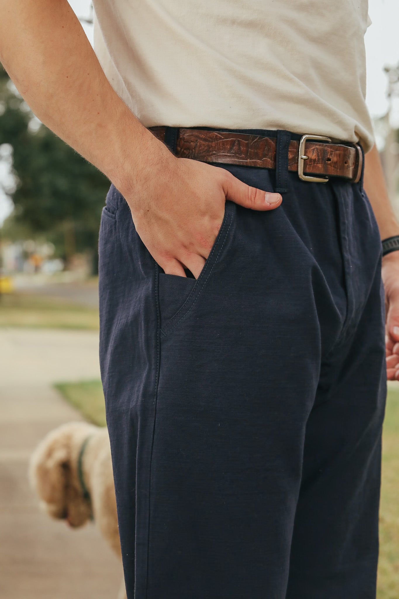 Person wearing navy pants with a brown belt outdoors