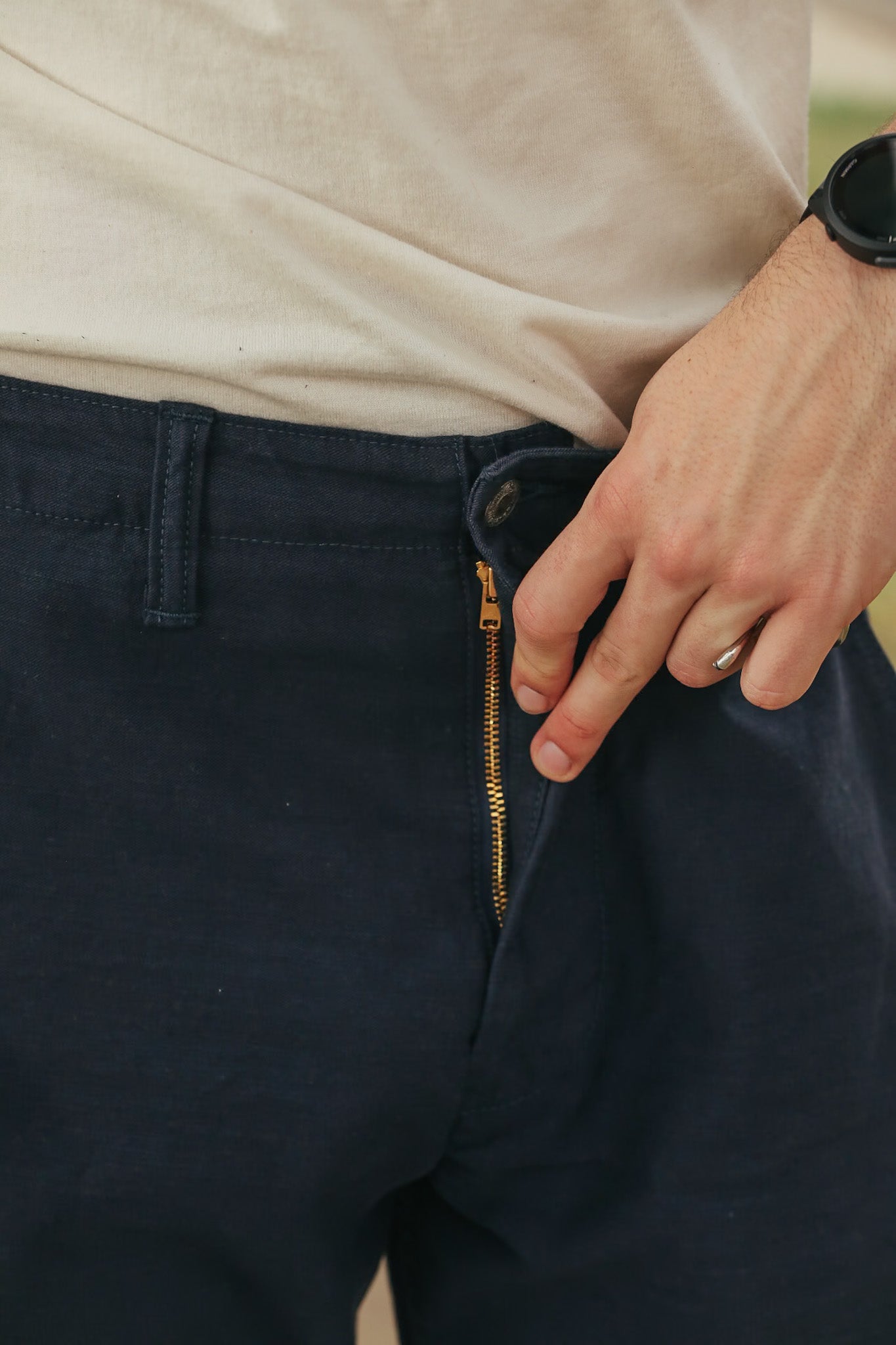Navy pants with a gold zipper being adjusted by a hand.