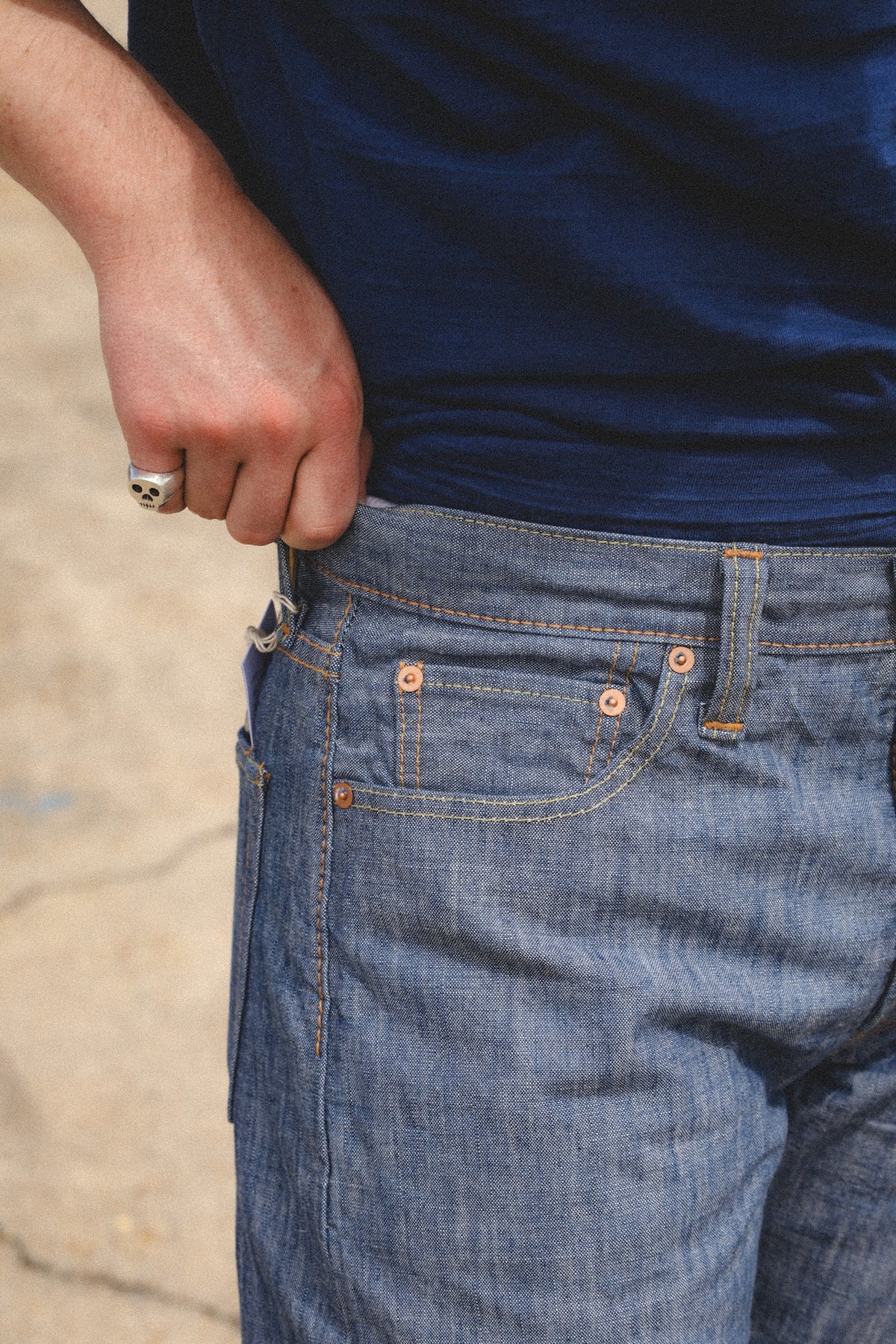 Close-up of a person wearing blue denim jeans and a navy blue t-shirt, pulling the shirt down slightly to show the fit of the jeans.