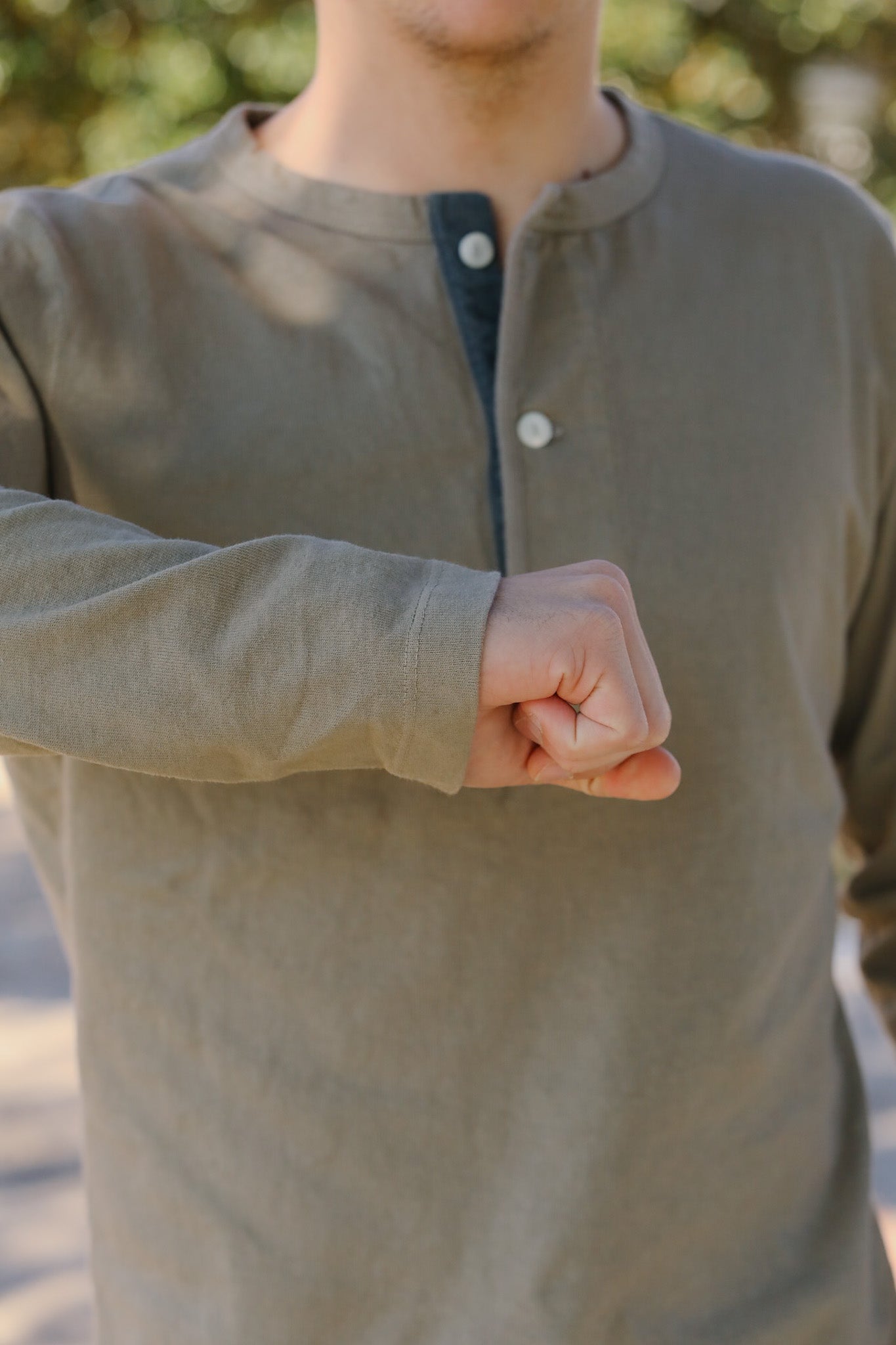 Person wearing a green long-sleeve shirt with a blurred natural background
