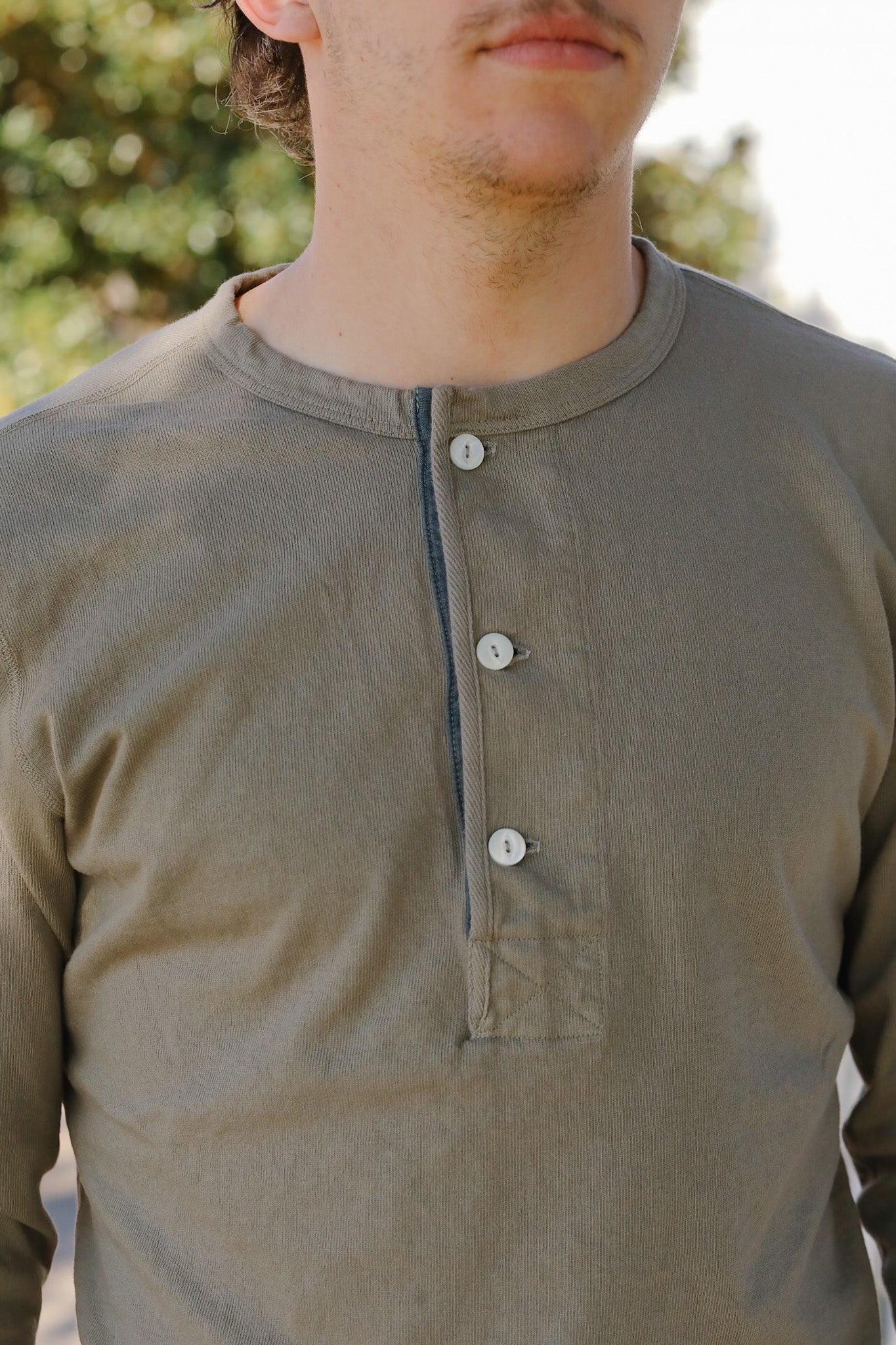 Person wearing a brown long-sleeve shirt with buttons, standing outdoors.