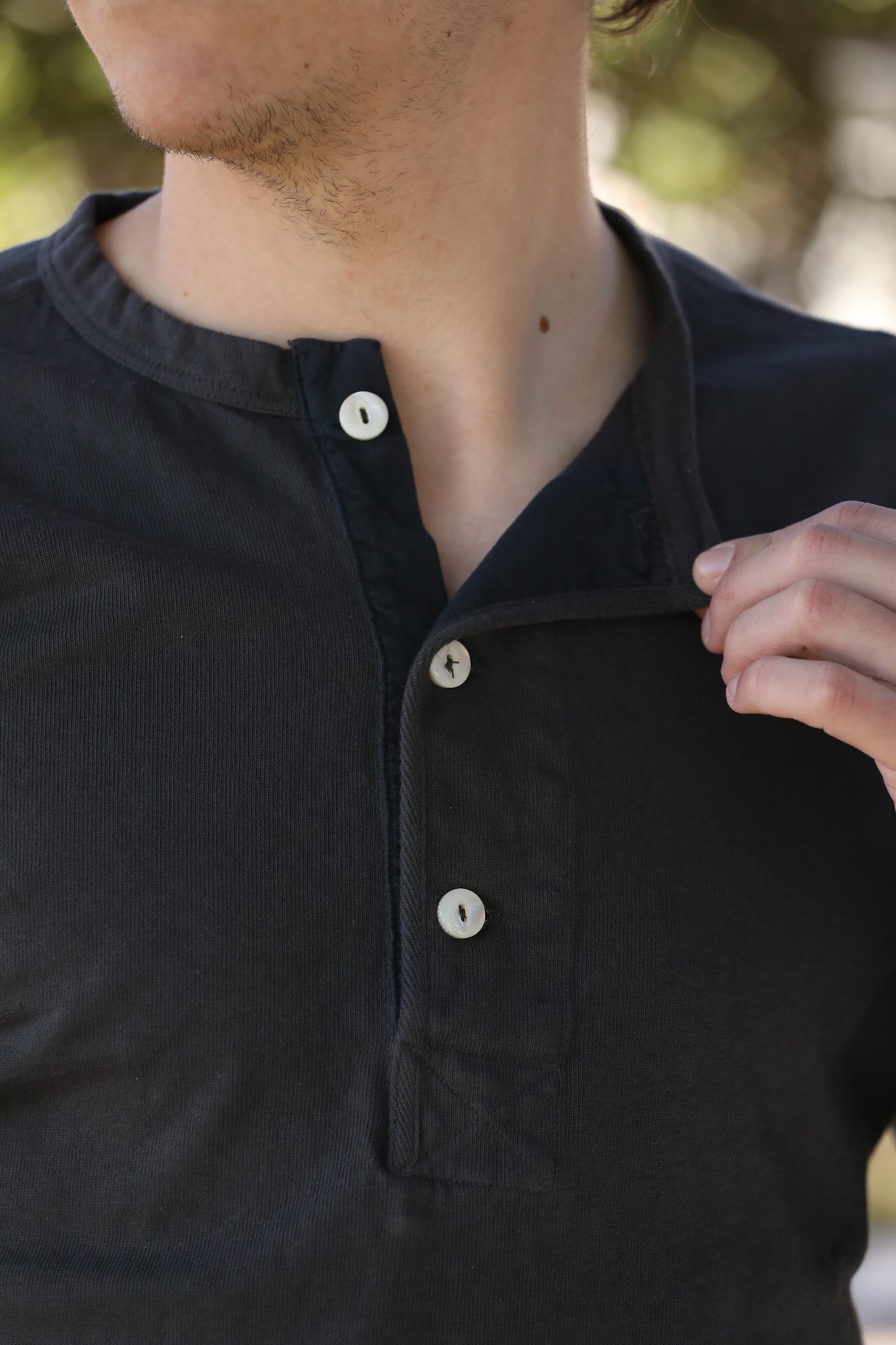 Close-up of a person wearing a black button-up shirt with a blurred background