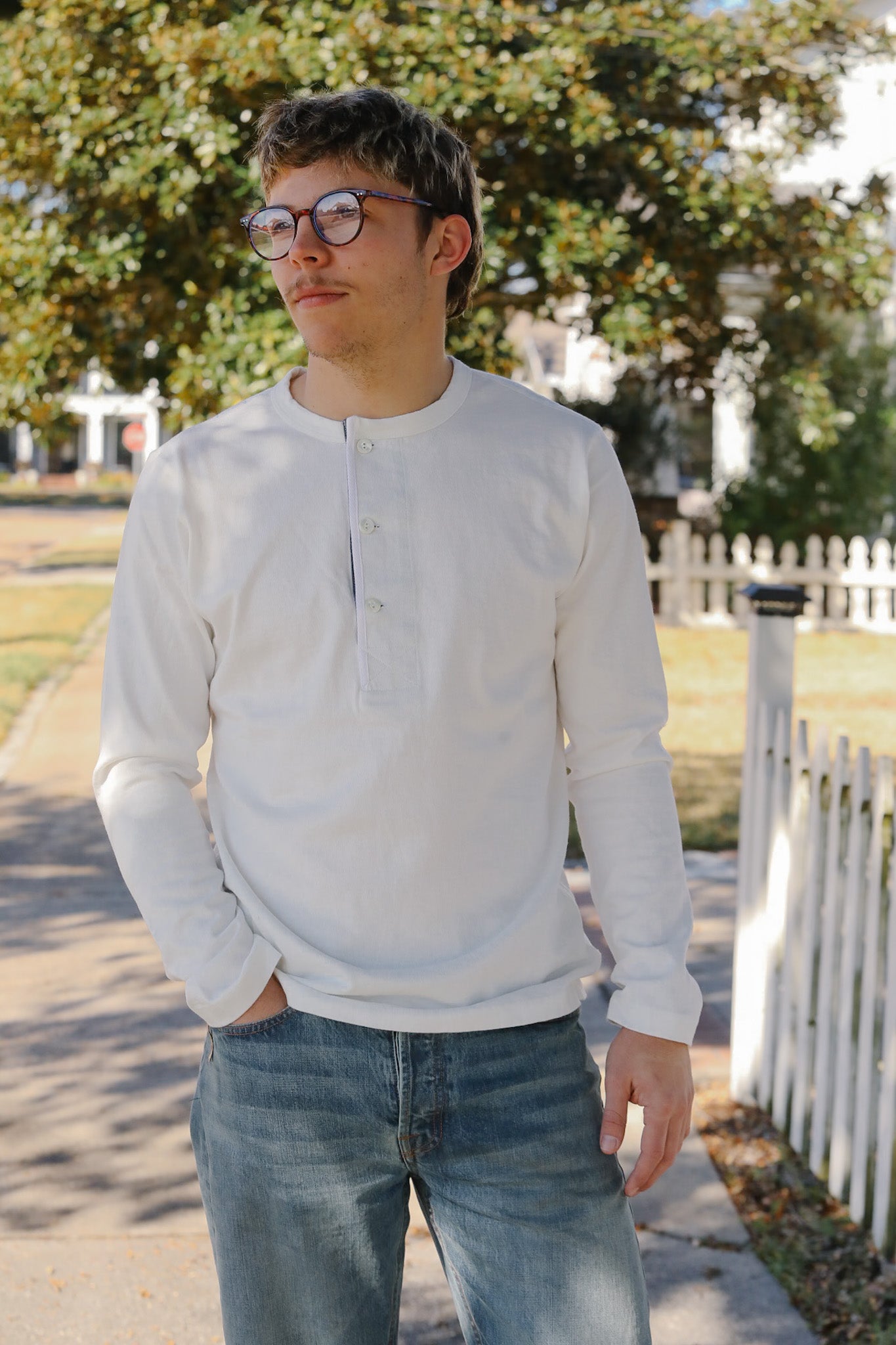 Person wearing a light gray long-sleeve shirt and blue jeans standing outdoors.