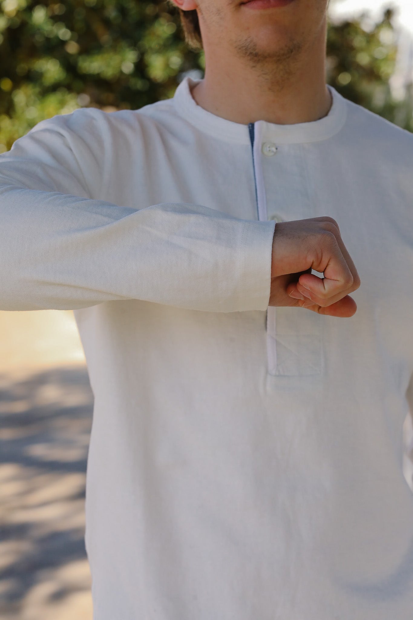 Person wearing a light-colored long-sleeve shirt with a blurred natural background