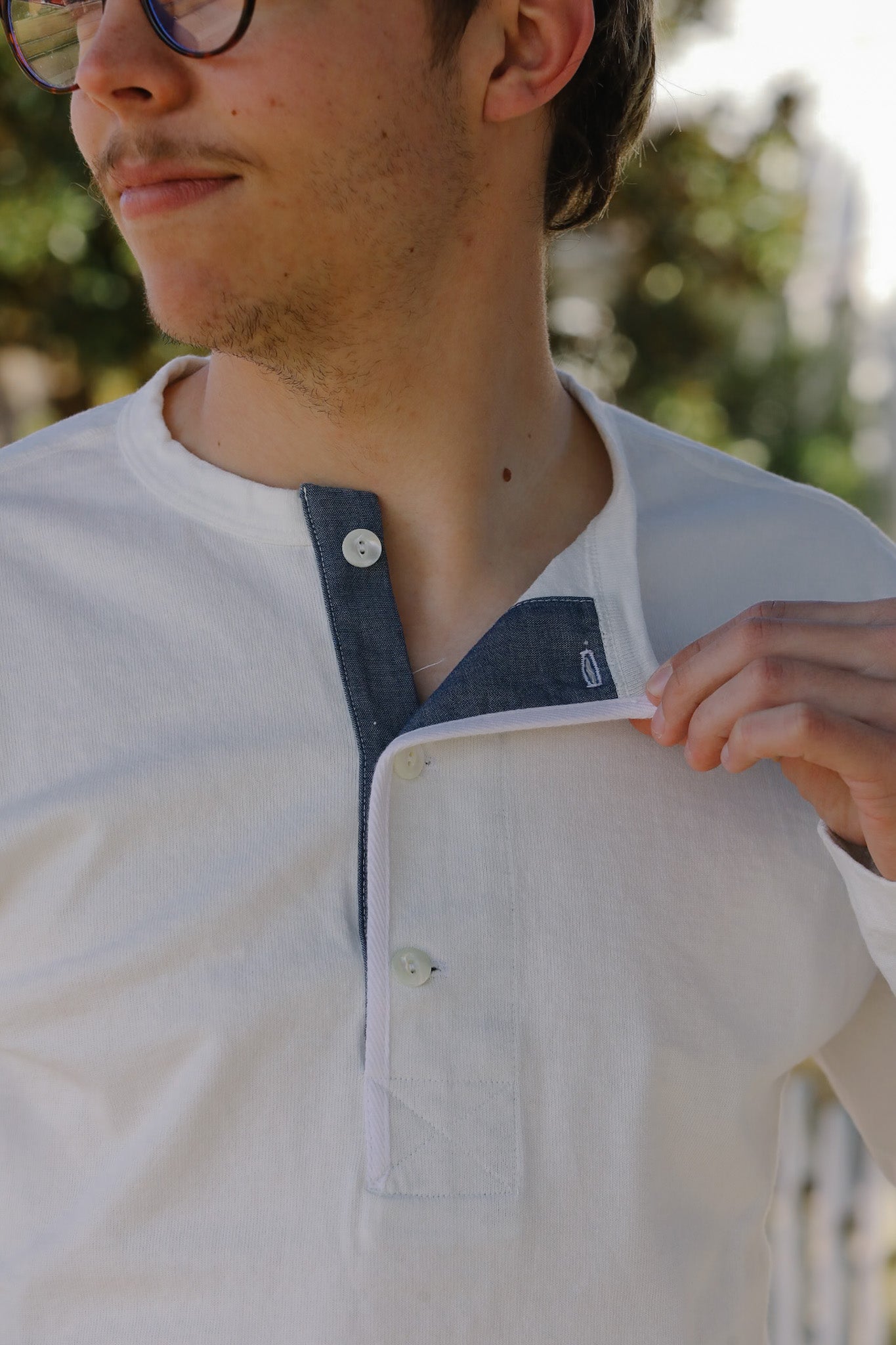 Person wearing a white shirt with a denim collar, outdoors.