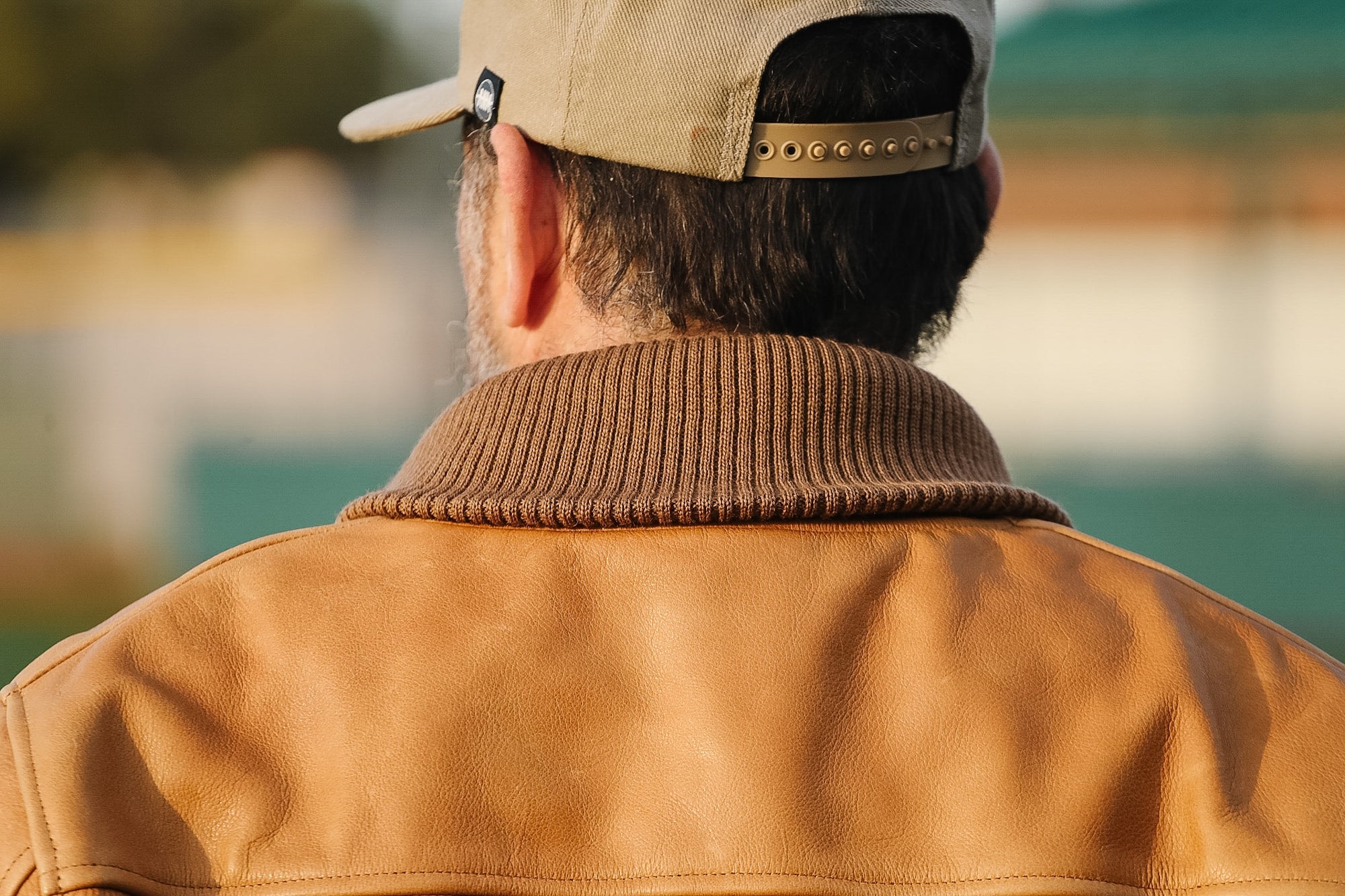 Person wearing a brown leather jacket and cap with a blurred natural background