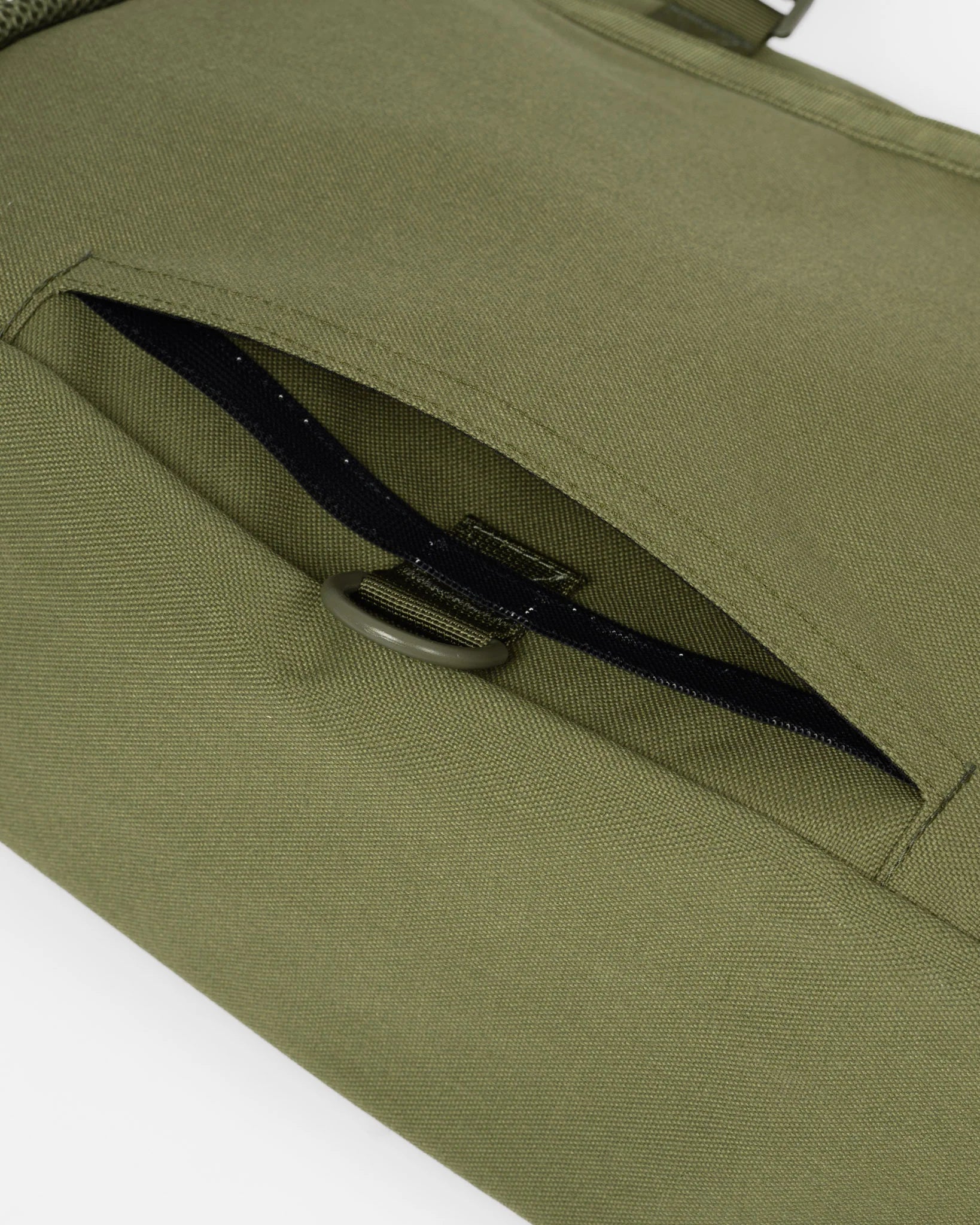 Close-up of an olive green canvas bag with a zippered pocket and a dark metal D-ring closure.