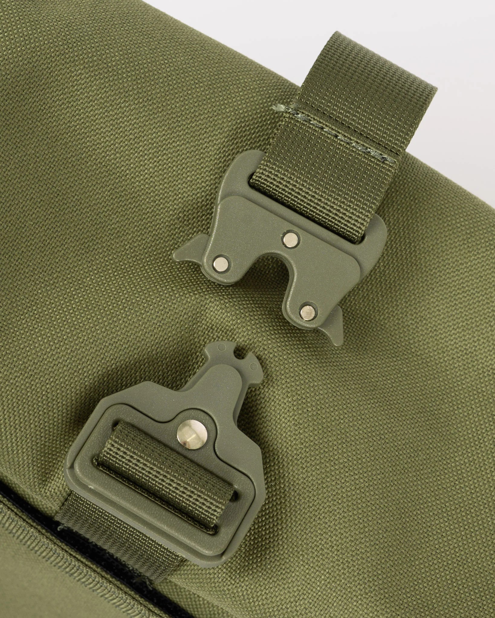 Close-up of an olive green canvas bag with two matching plastic buckle straps on a light gray background.