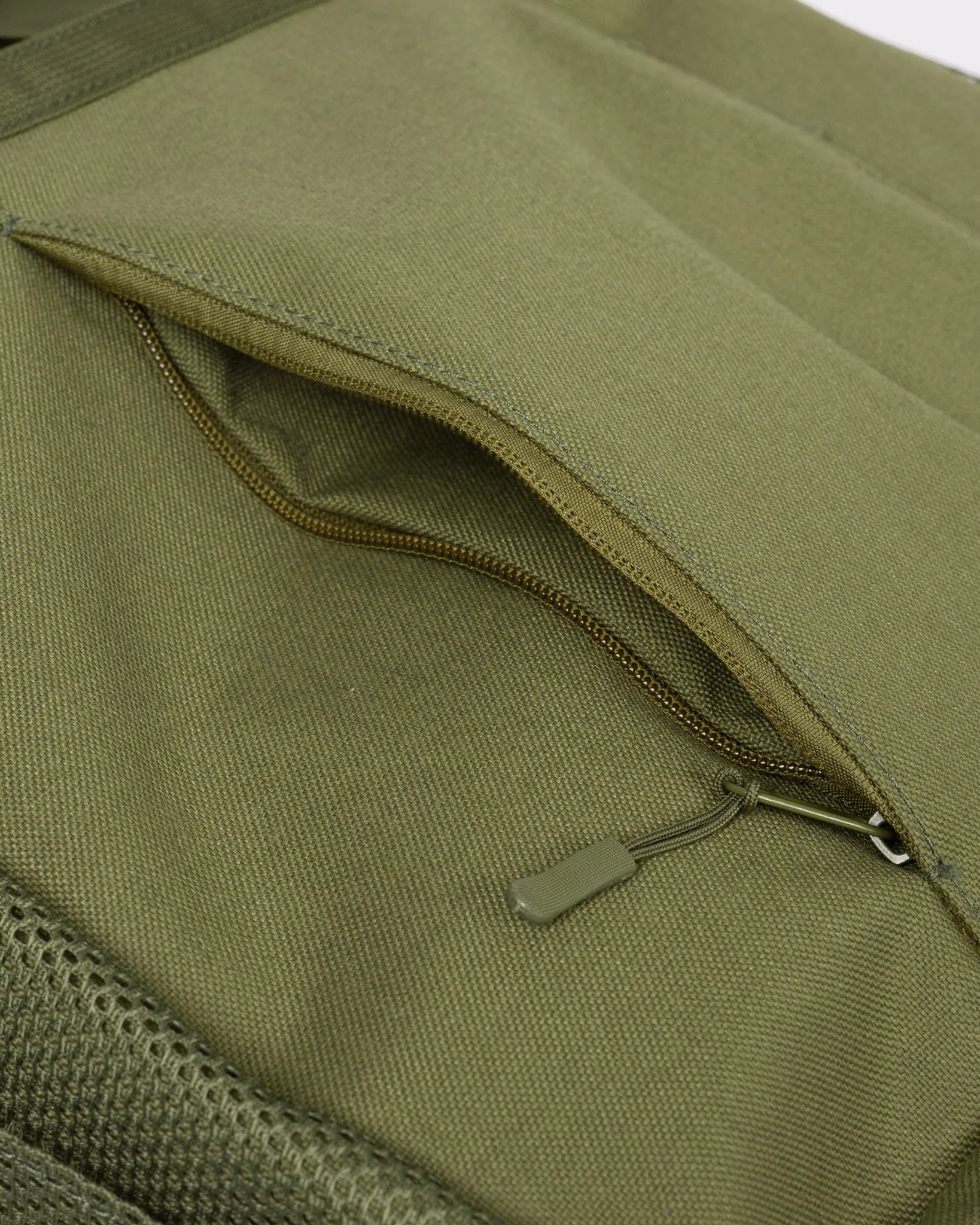 Close-up of an olive green canvas bag showing a zippered pocket with a matching olive green zipper pull.