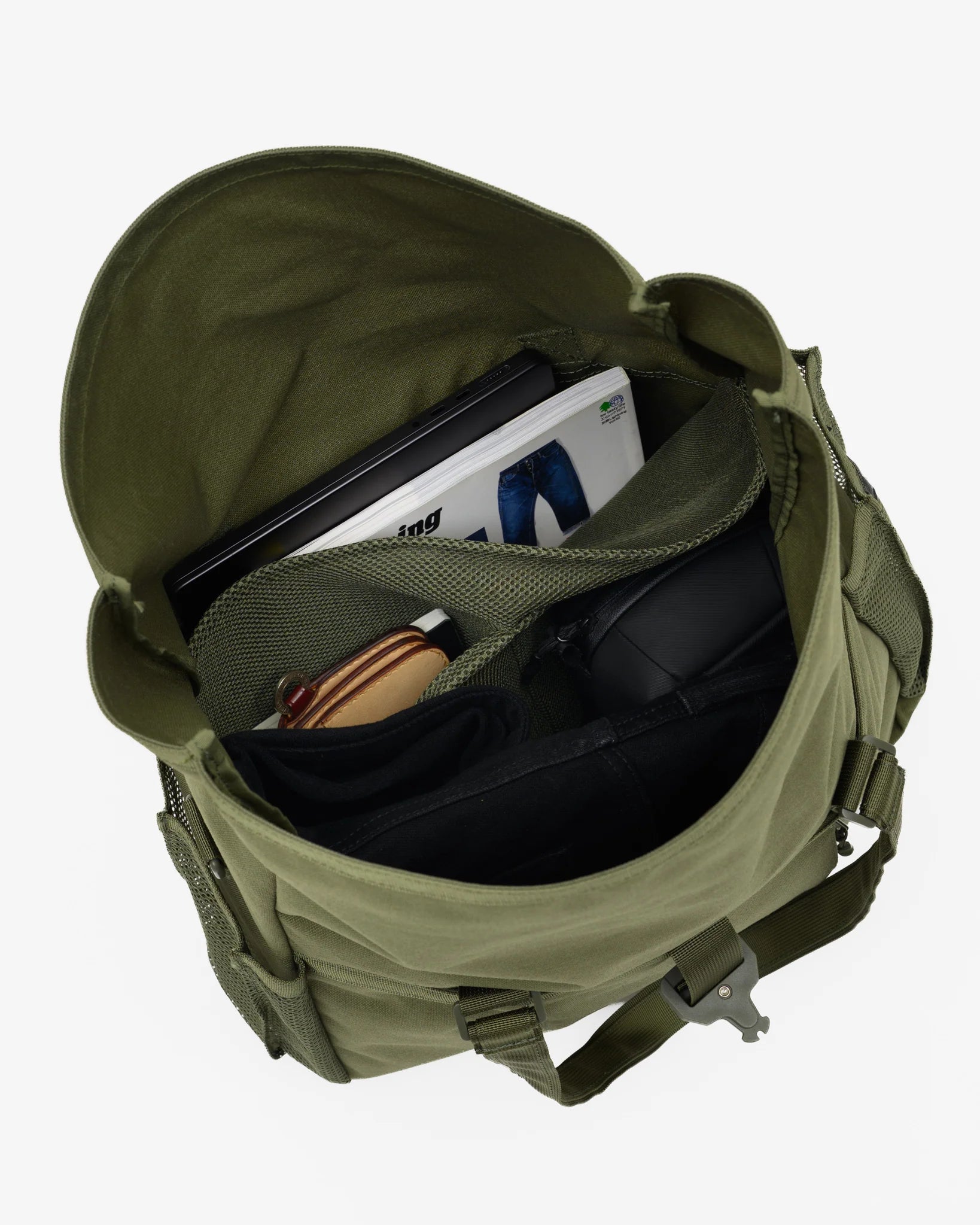 An olive green canvas duffel bag shown from an overhead angle, open to reveal its interior compartments filled with travel accessories like a laptop, notebook, and headphones, set against a plain light gray background.