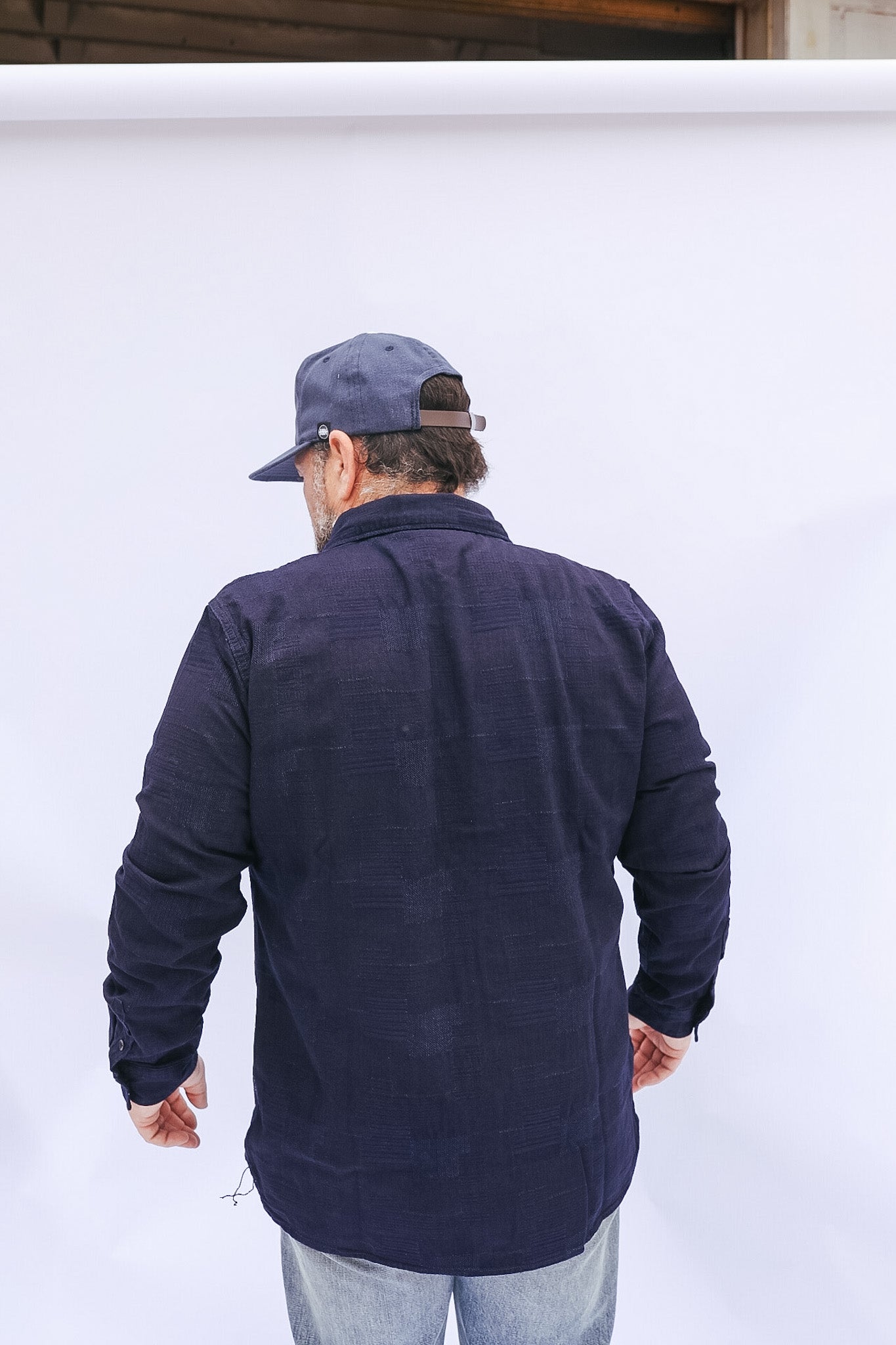 Man wearing a navy blue jacket and cap standing against a white background