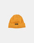 Old gold wool knit watch cap with leather patch label laid flat on white background