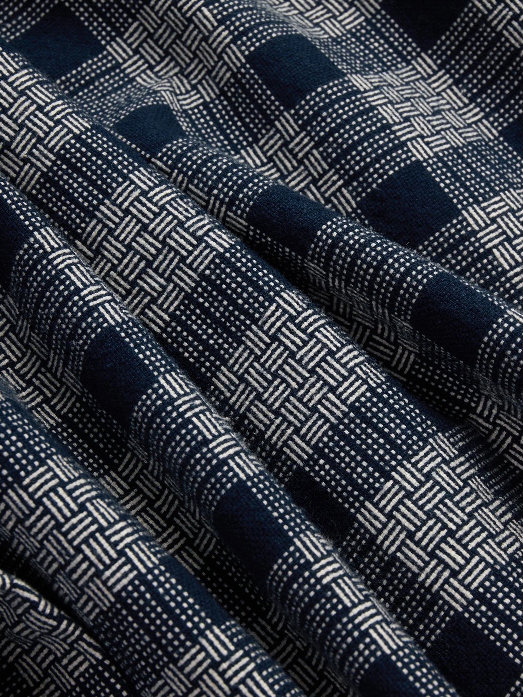 A close-up of a woven fabric with a navy blue and off-white basketweave pattern, shown in soft folds.