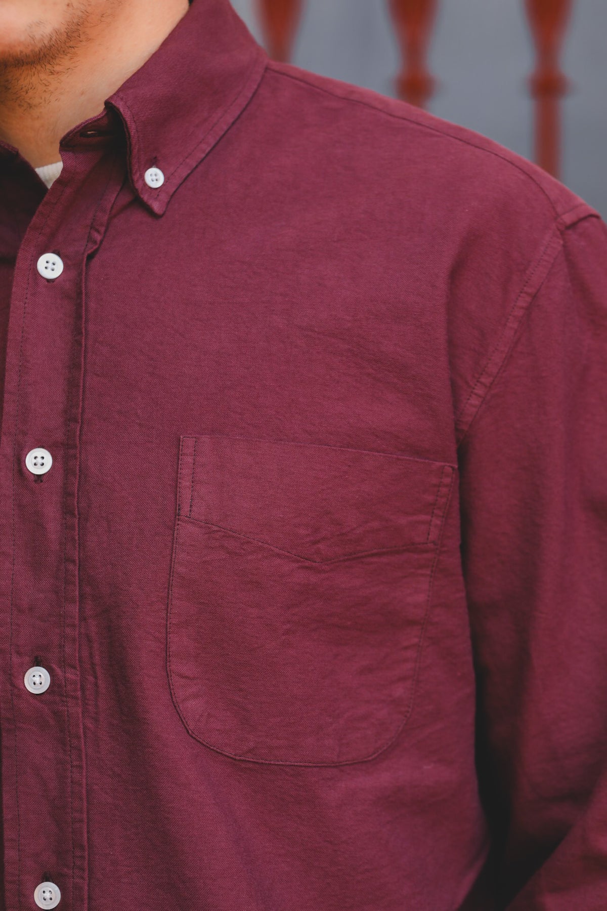 Close-up of a man wearing a burgundy button-down shirt with a chest pocket and white buttons.