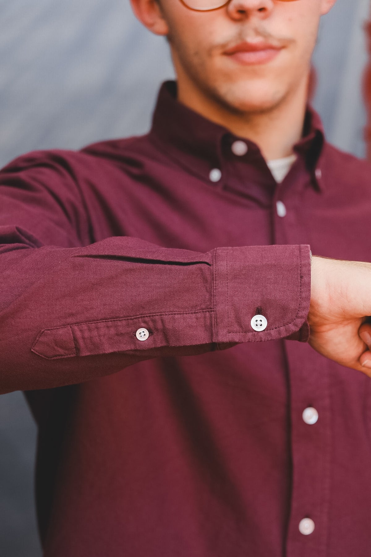 A close-up of a man wearing a burgundy long-sleeve button-down shirt, showing the fabric texture and white buttons on the cuff.