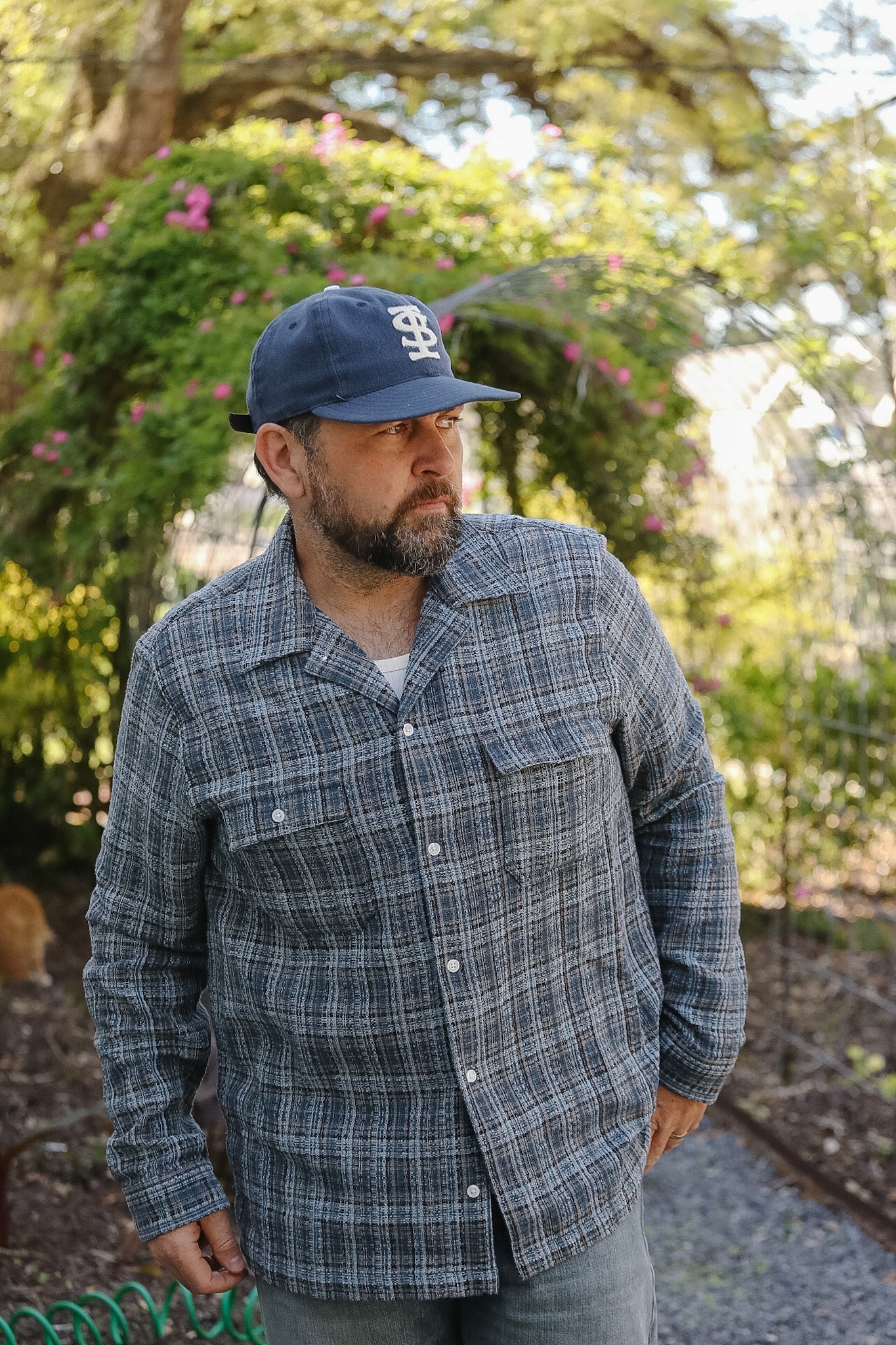 Man wearing a plaid shirt and cap in a garden setting