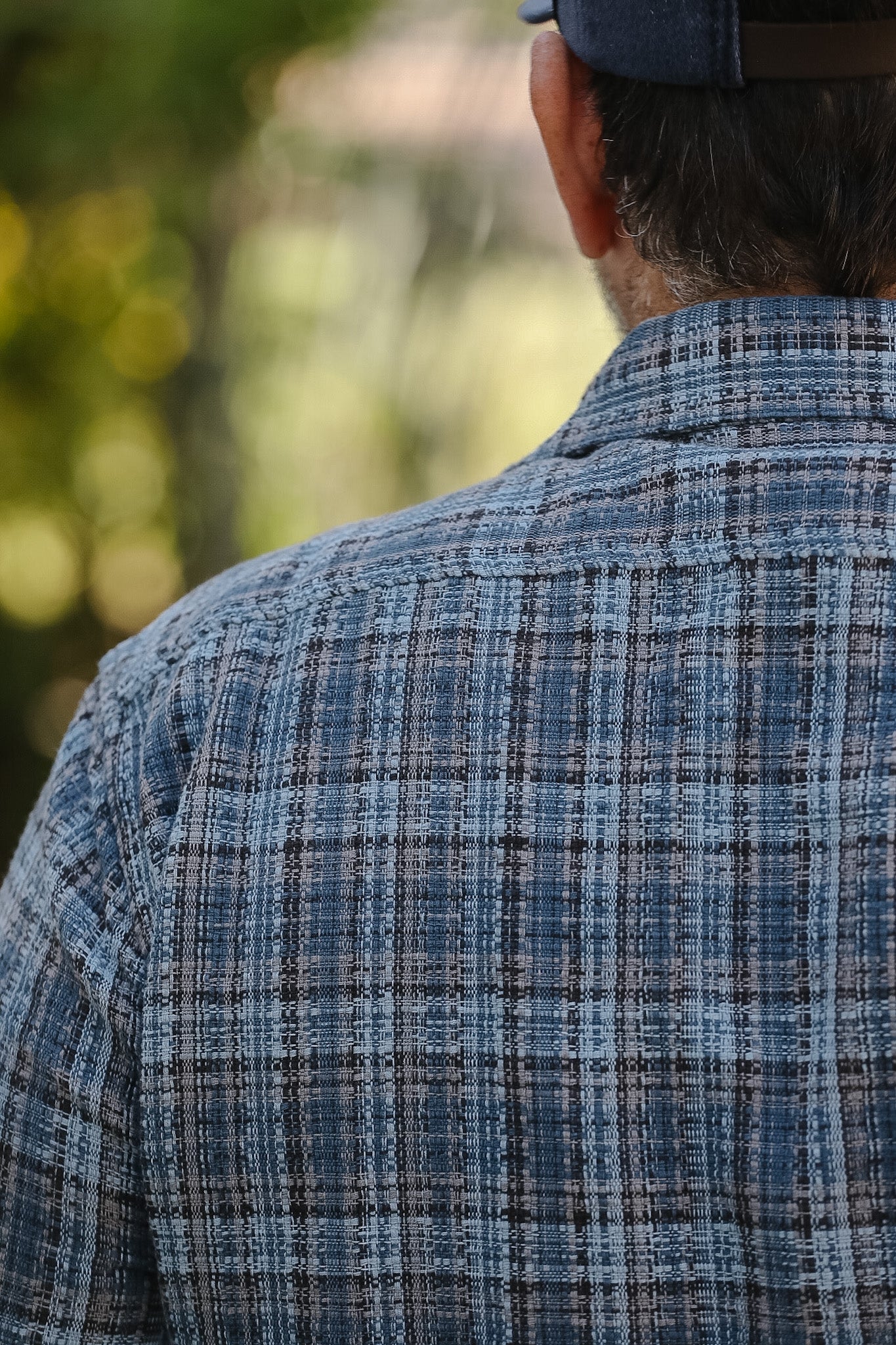 Person wearing a blue plaid shirt with a blurred natural background