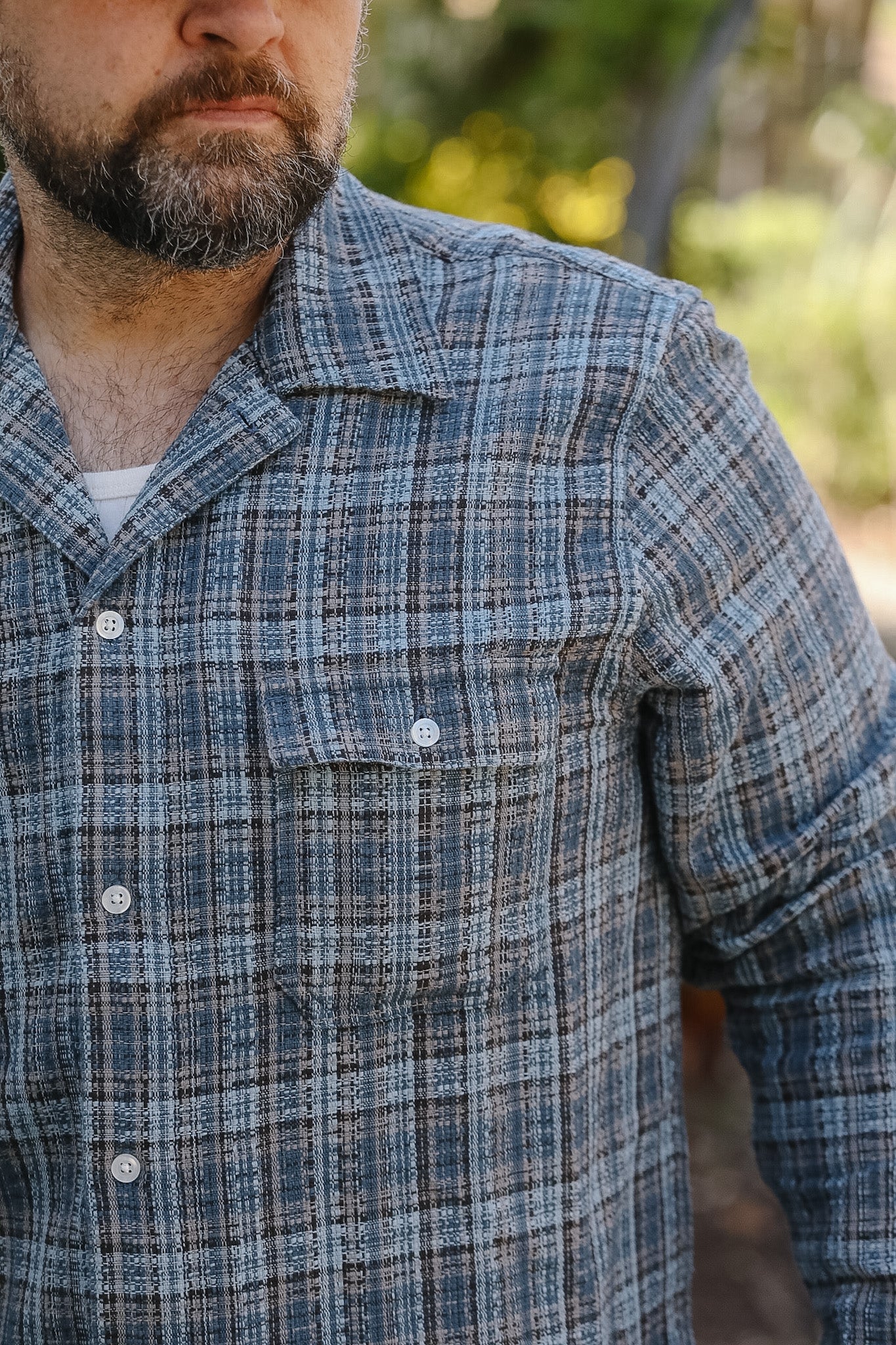Man wearing a blue plaid shirt with a blurred outdoor background