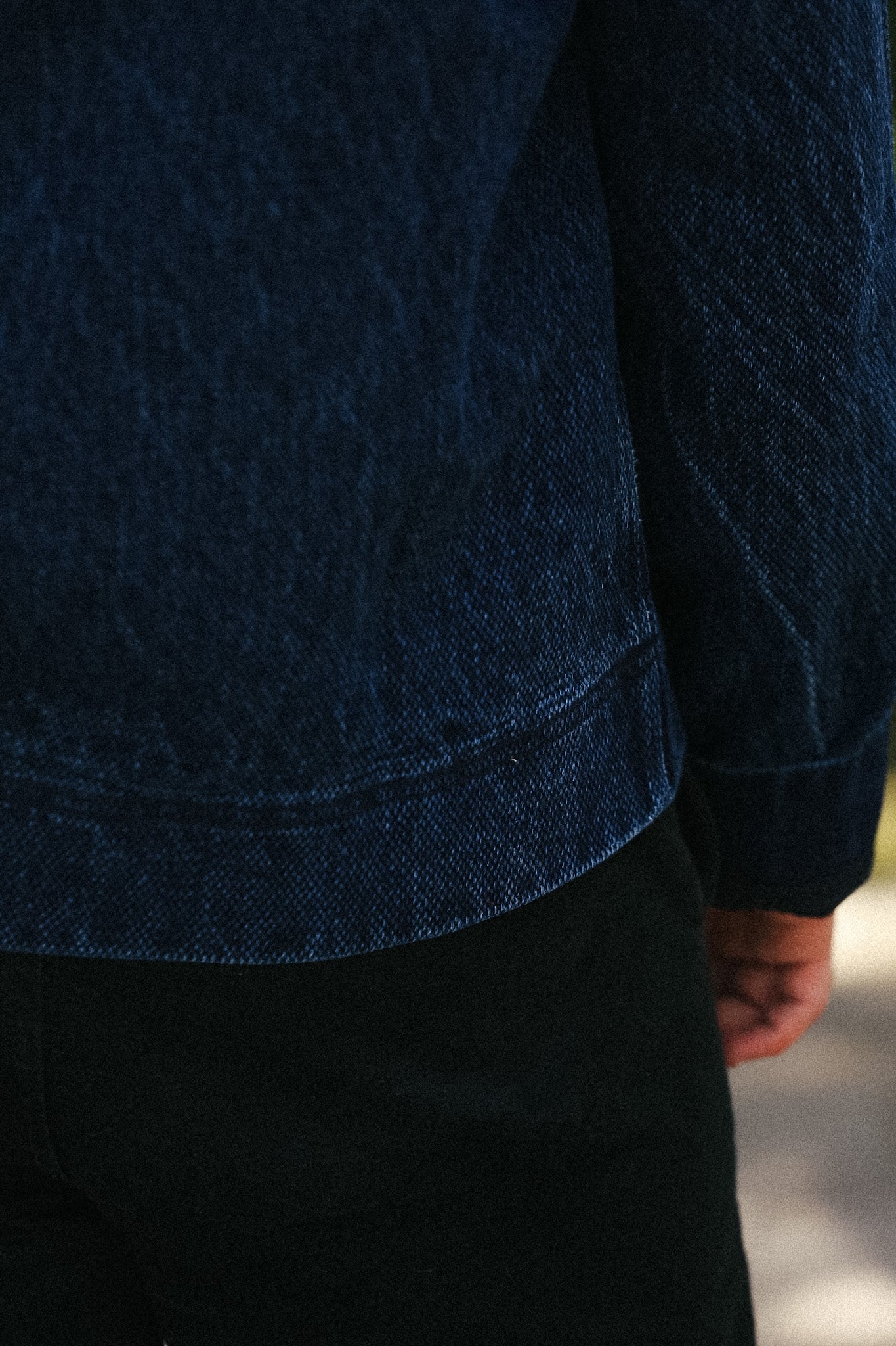 Close-up of a person wearing a dark navy blue textured jacket or overshirt with black pants, showing the fabric texture and cuff detail.