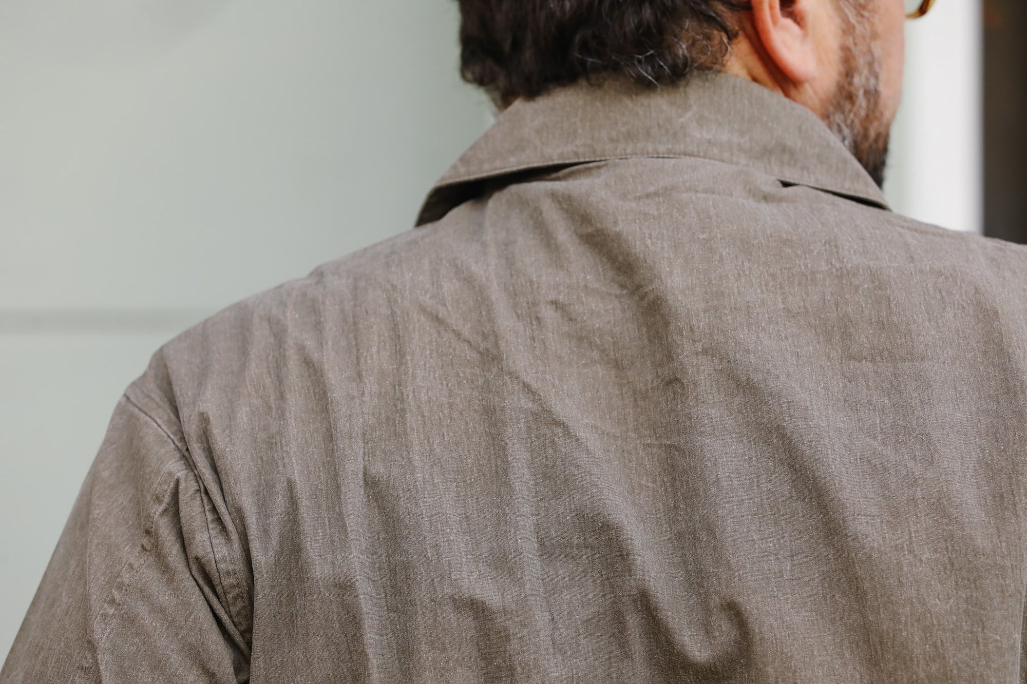 Back view of a person wearing a brown jacket with a neutral background