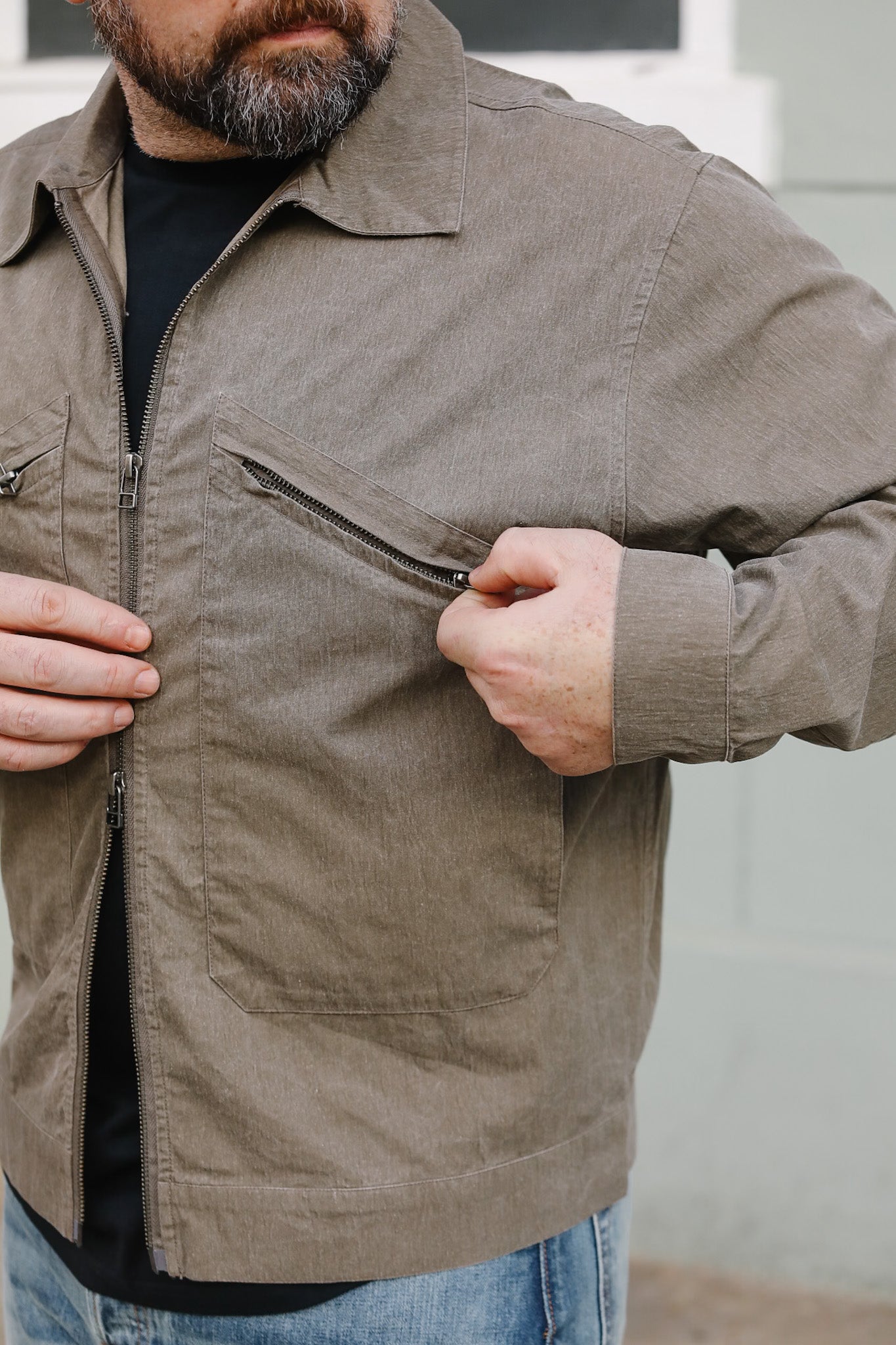Person wearing a brown jacket with a zipper, standing against a neutral background