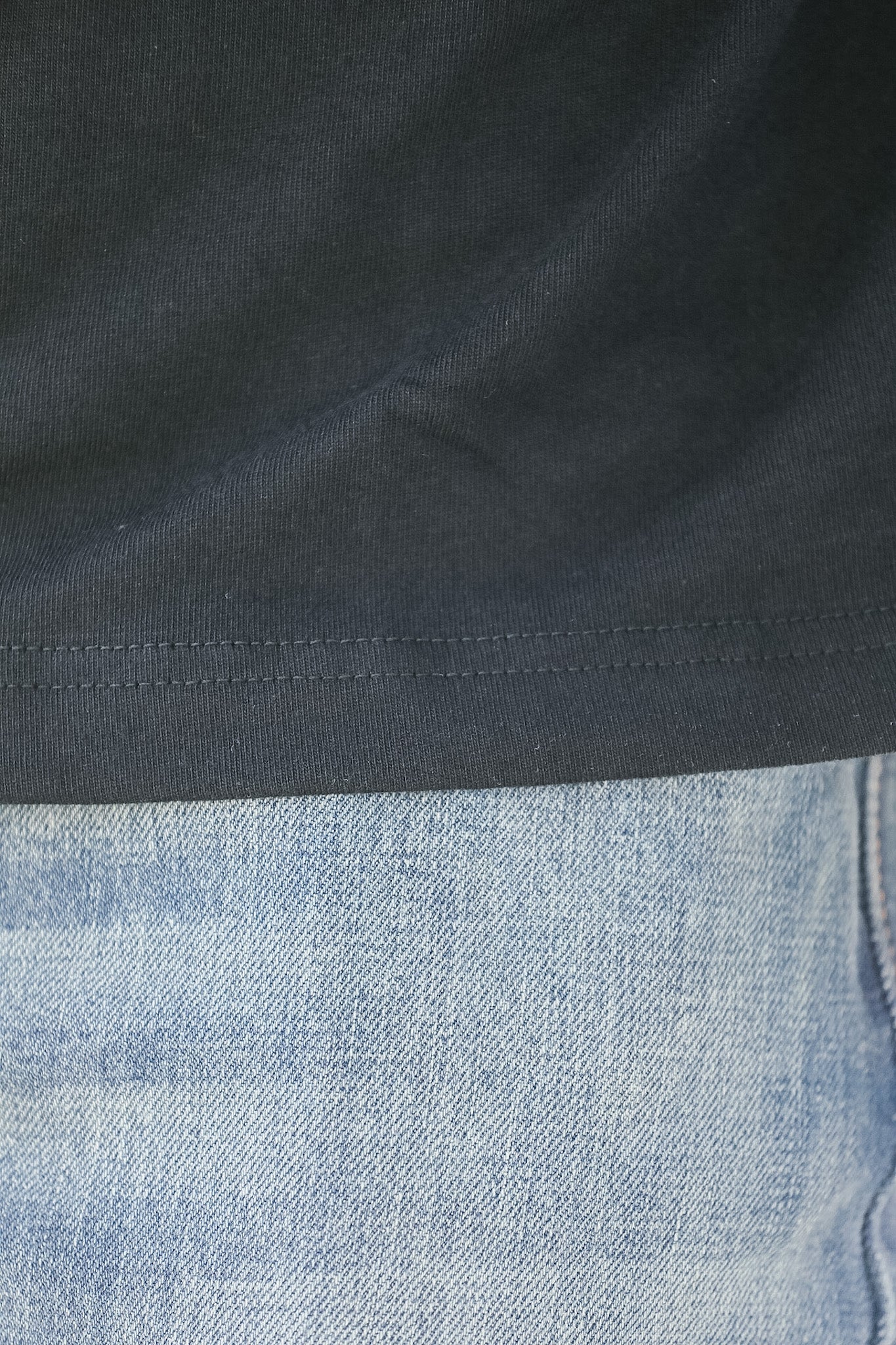 Close-up of a dark fabric surface with a light blue denim fabric underneath.
