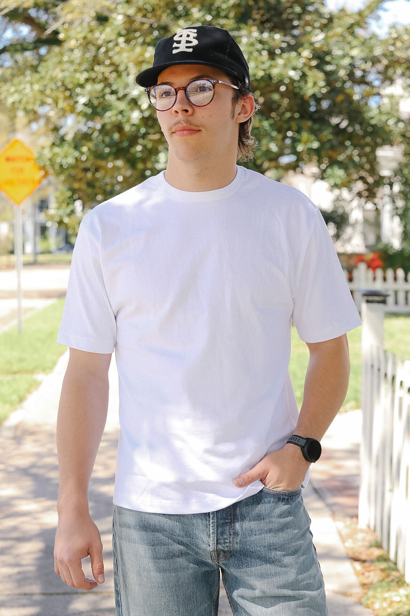 Person wearing a white t-shirt, black cap, and glasses outdoors.