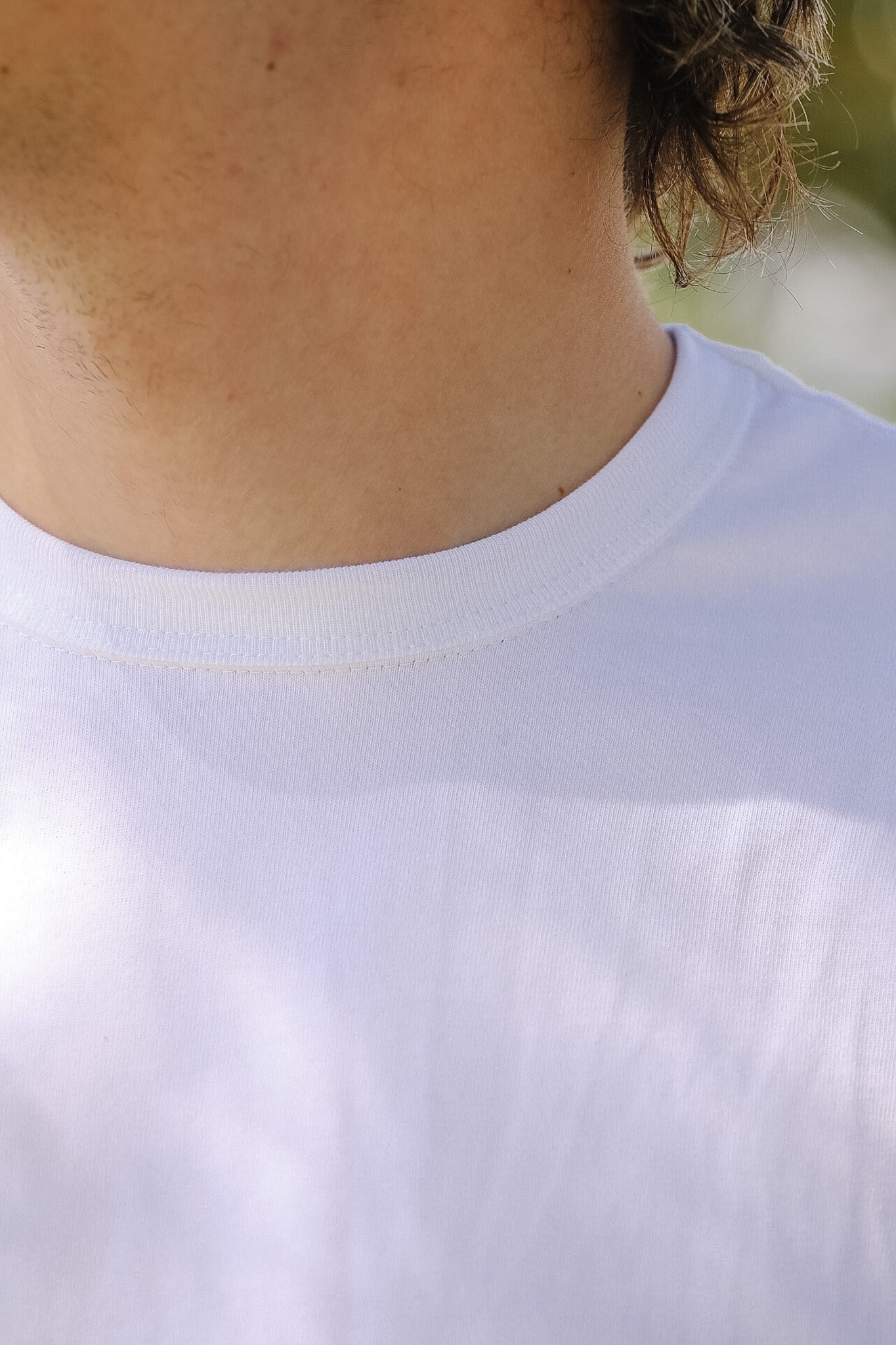 Close-up of a person wearing a plain white t-shirt with a blurred background