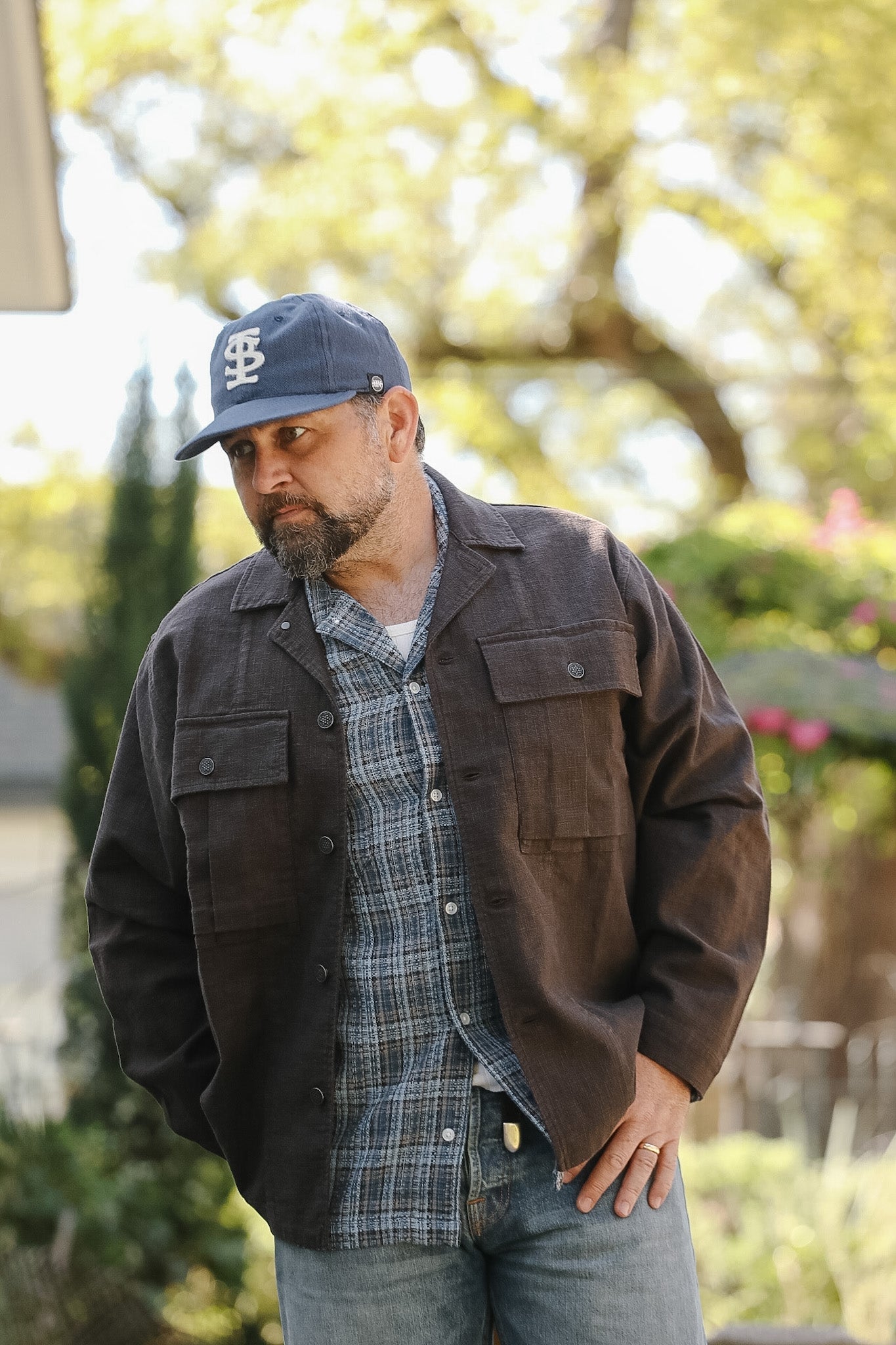 Man wearing a brown jacket and plaid shirt outdoors with blurred background