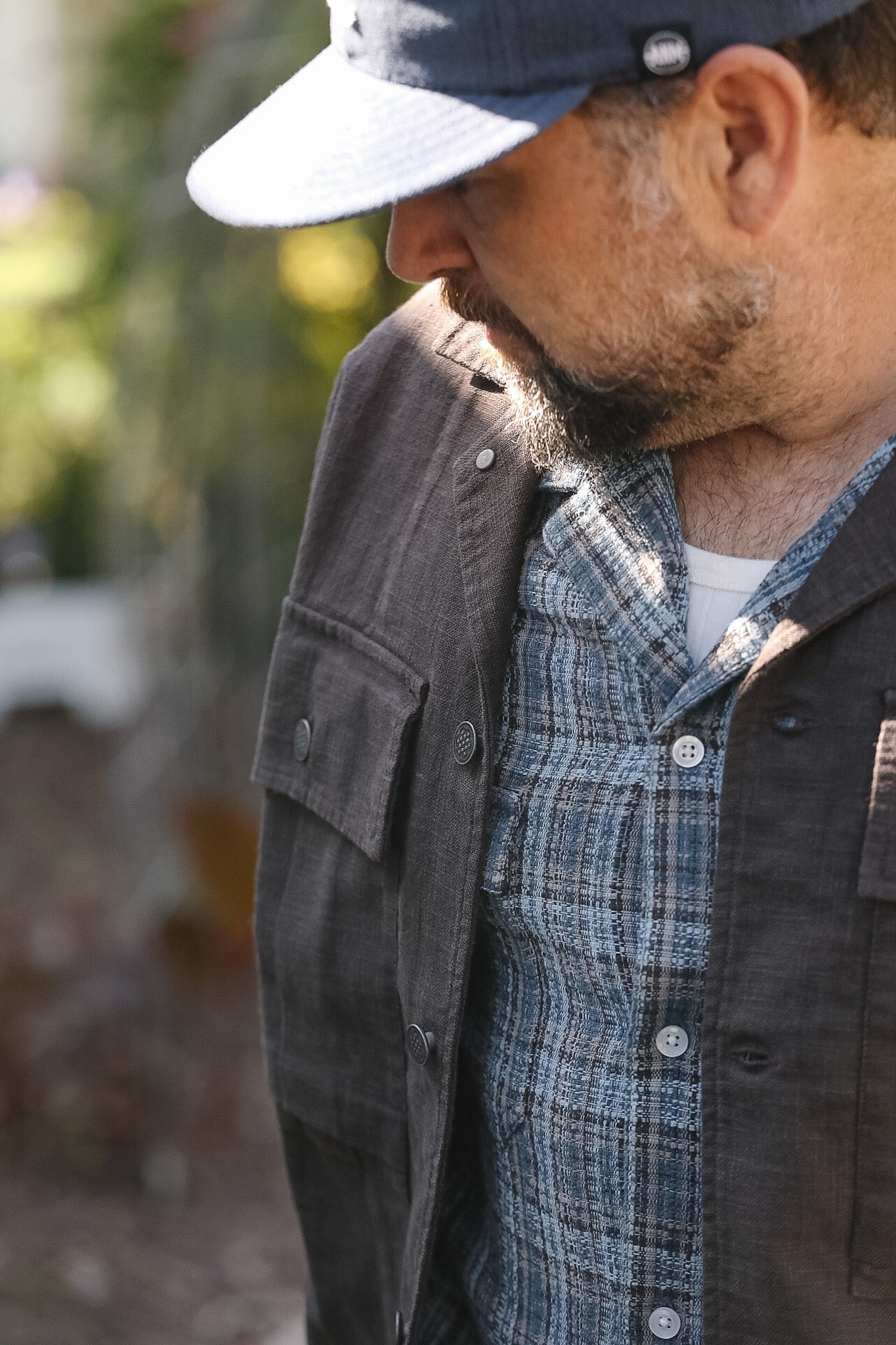 Man wearing a cap, dark jacket, and plaid shirt outdoors