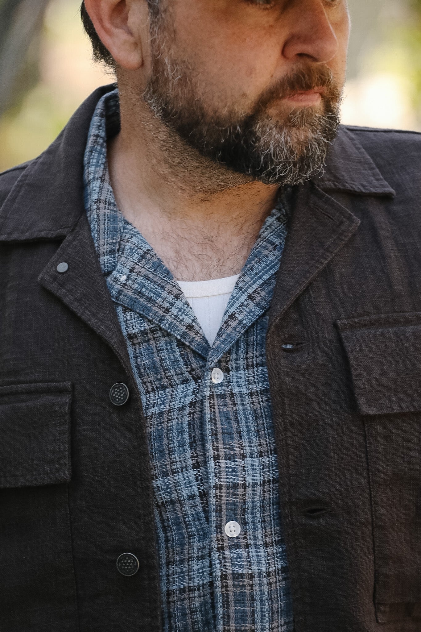 Man wearing a dark coat over a plaid shirt with a blurred background