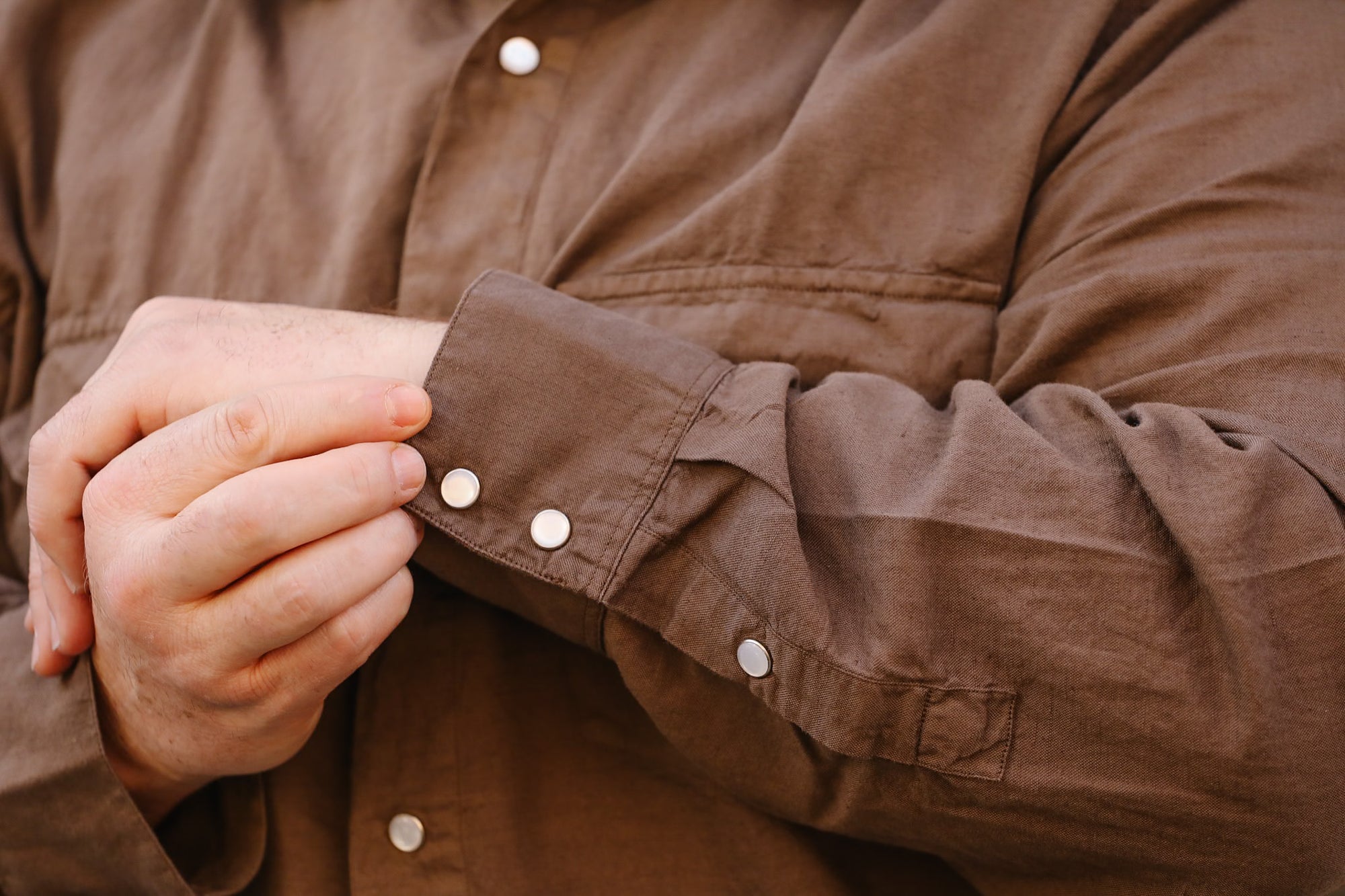 Close-up of a person wearing a brown jacket with rolled-up sleeves.
