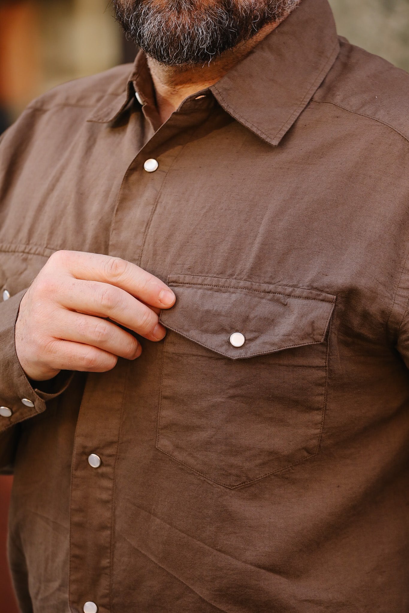 Close-up of a brown shirt with a pocket and buttons, worn by a person.
