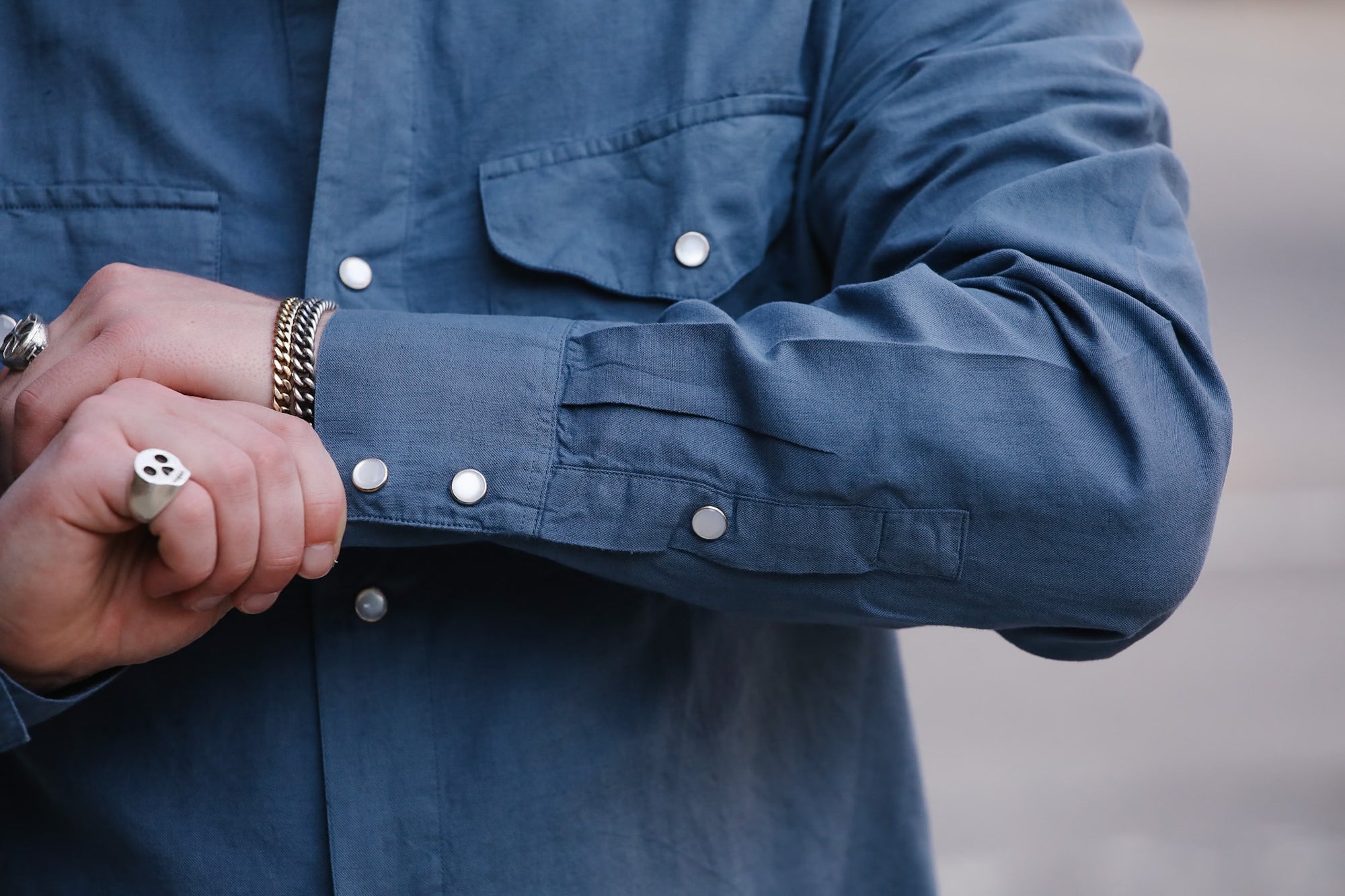Close-up of a person wearing a blue shirt with rolled-up sleeves, holding a phone.