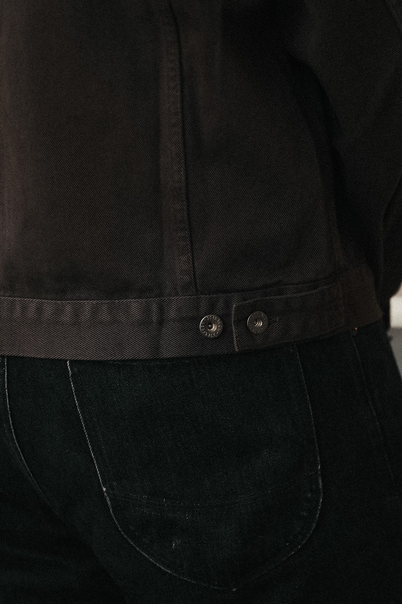 Close-up of a dark brown cropped jacket with a buttoned waistband, worn over black jeans.