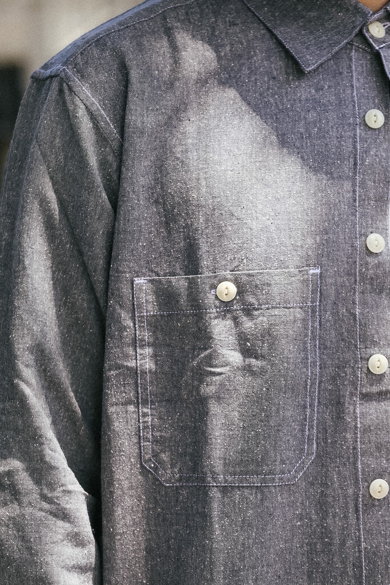 Close-up of a dark gray chambray button-up shirt with a chest pocket and white buttons.
