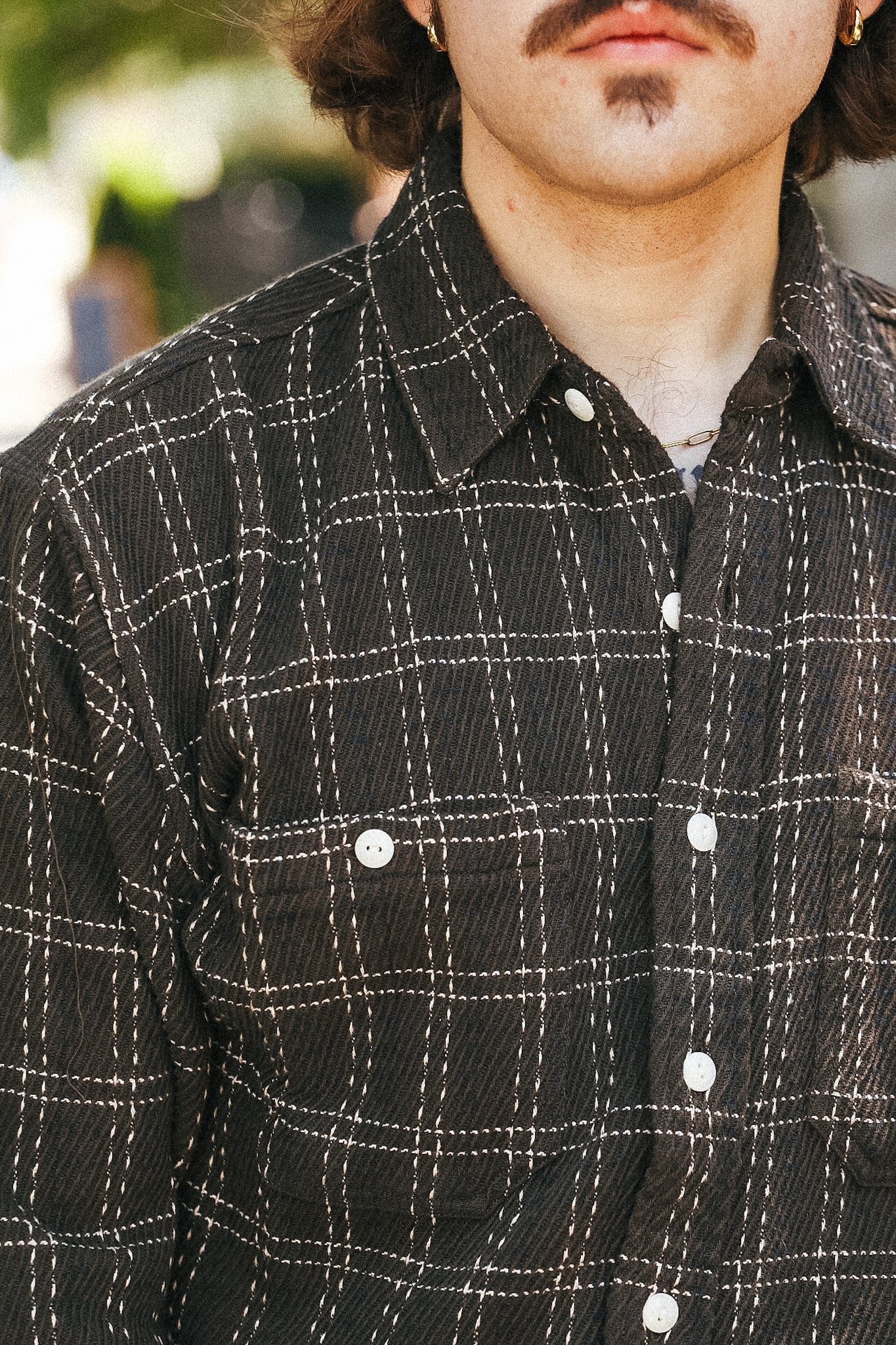 A close-up of a person wearing a dark charcoal gray plaid button-down shirt with white contrast stitching and white buttons.