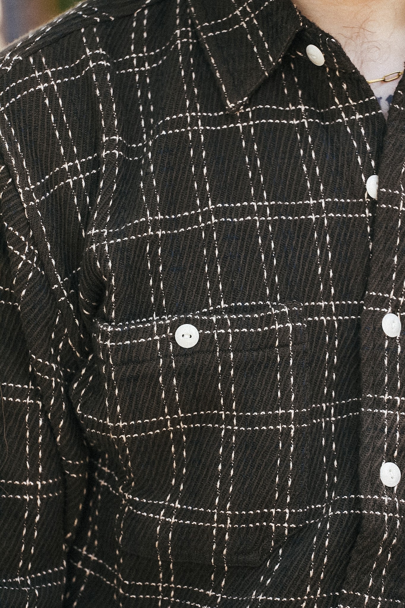 Close-up of a black corduroy button-up shirt with a white windowpane plaid pattern and white buttons.