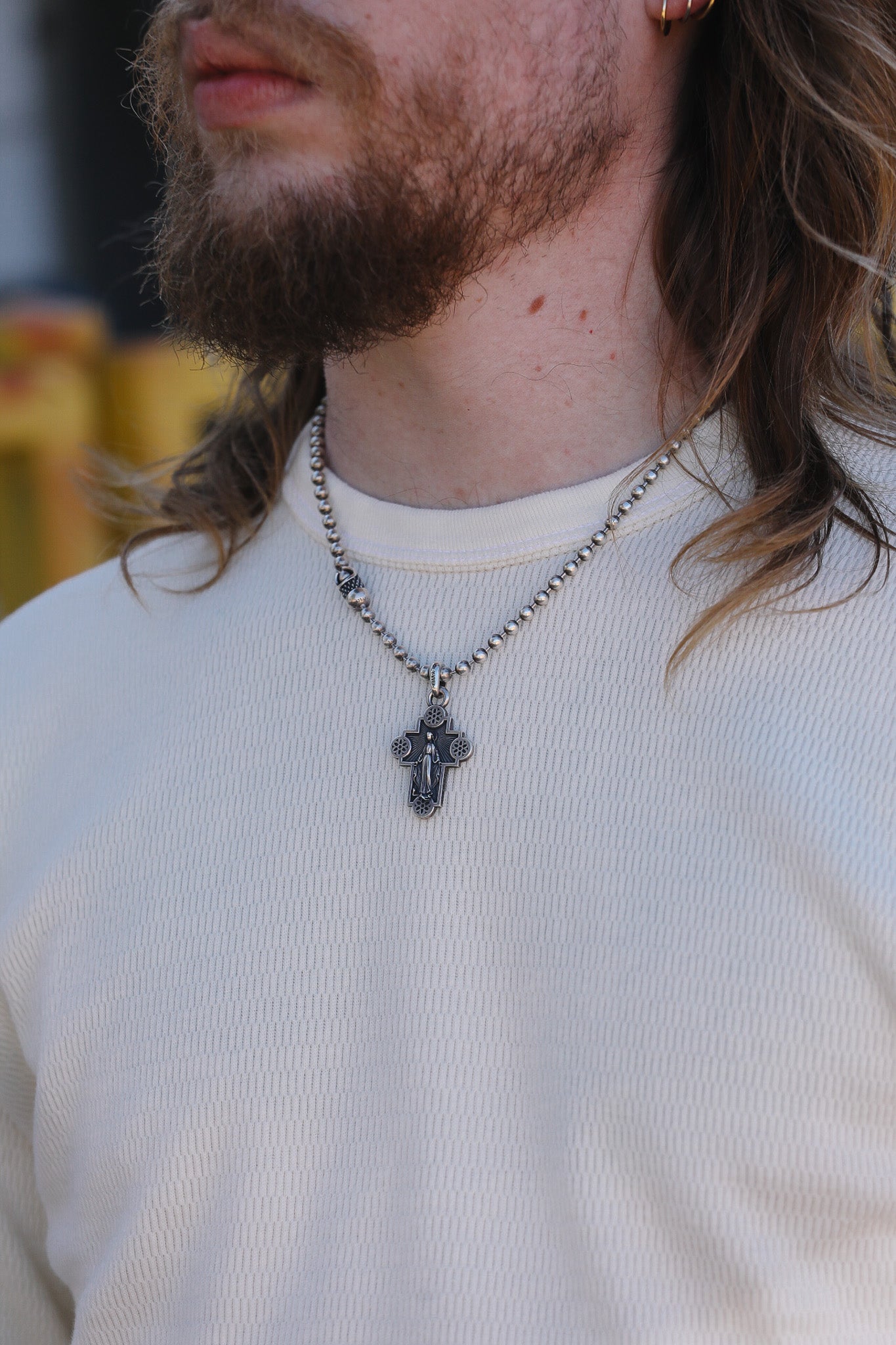 Person wearing a necklace with a cross pendant on a blurred background