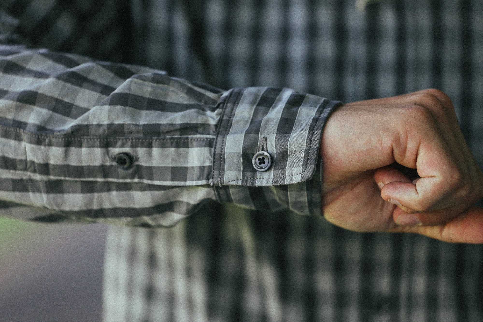 Close-up of a person's hand and wrist wearing a gray and black checkered long-sleeve button-up shirt.