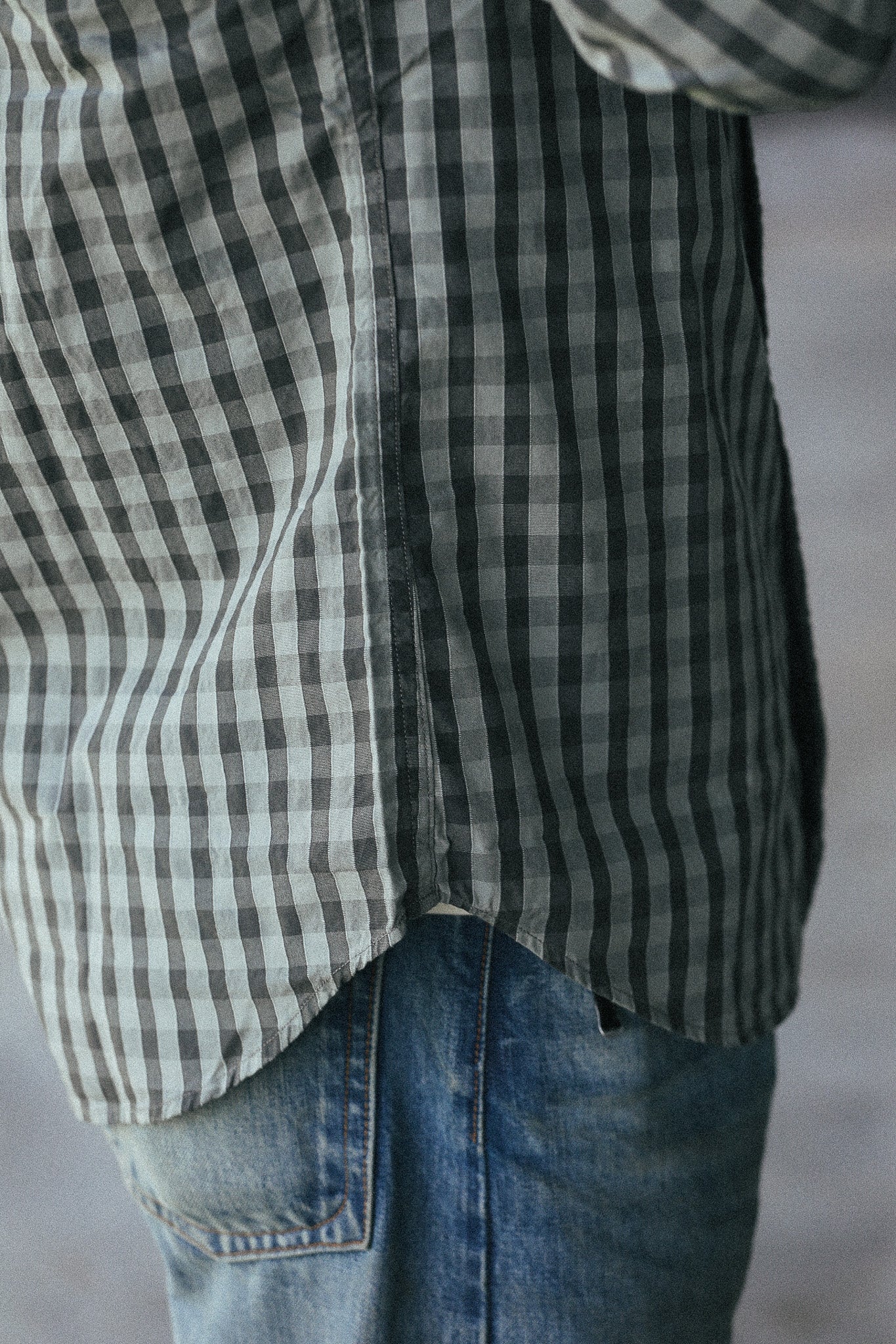 Close-up of a person wearing a black and white gingham plaid shirt tucked into blue jeans.