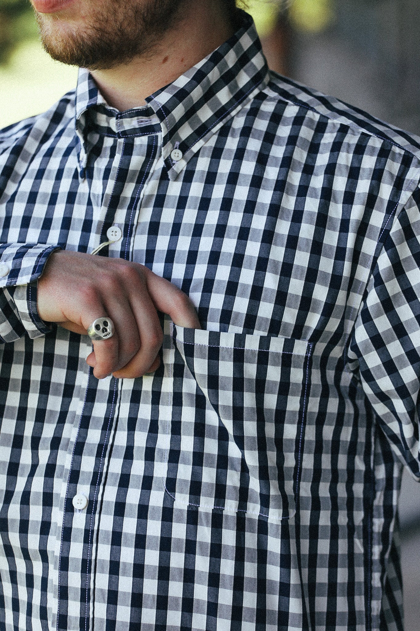 A close-up of a man wearing a black and white gingham check button-down shirt, with his hand resting on his chest pocket.