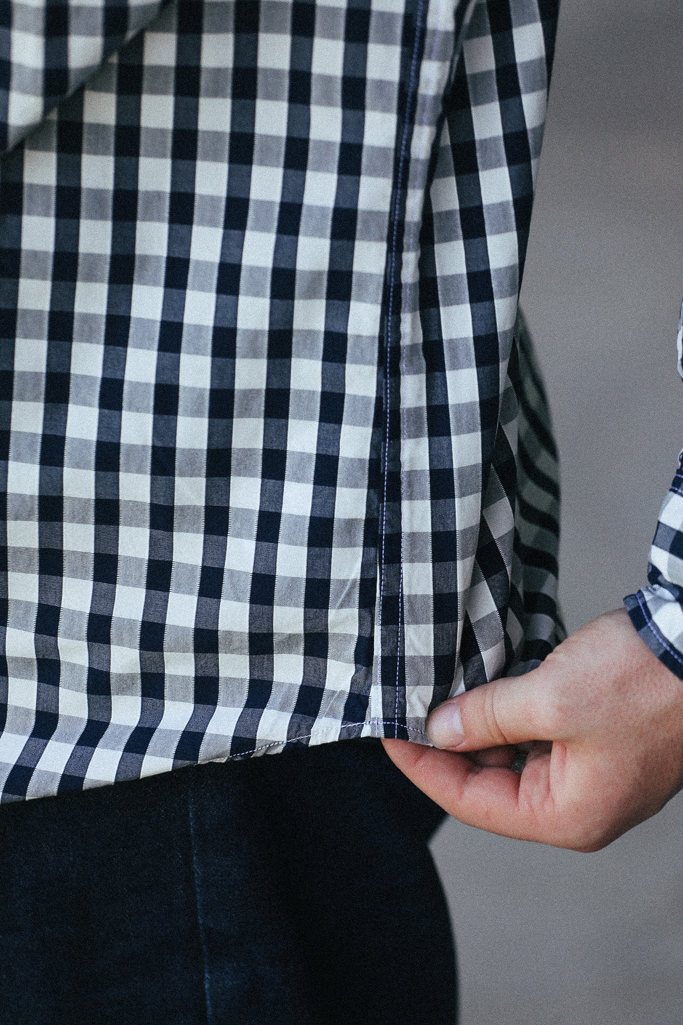 Close-up of a person wearing a black and white gingham plaid shirt, pulling the hem slightly to show the fabric and dark pants underneath.