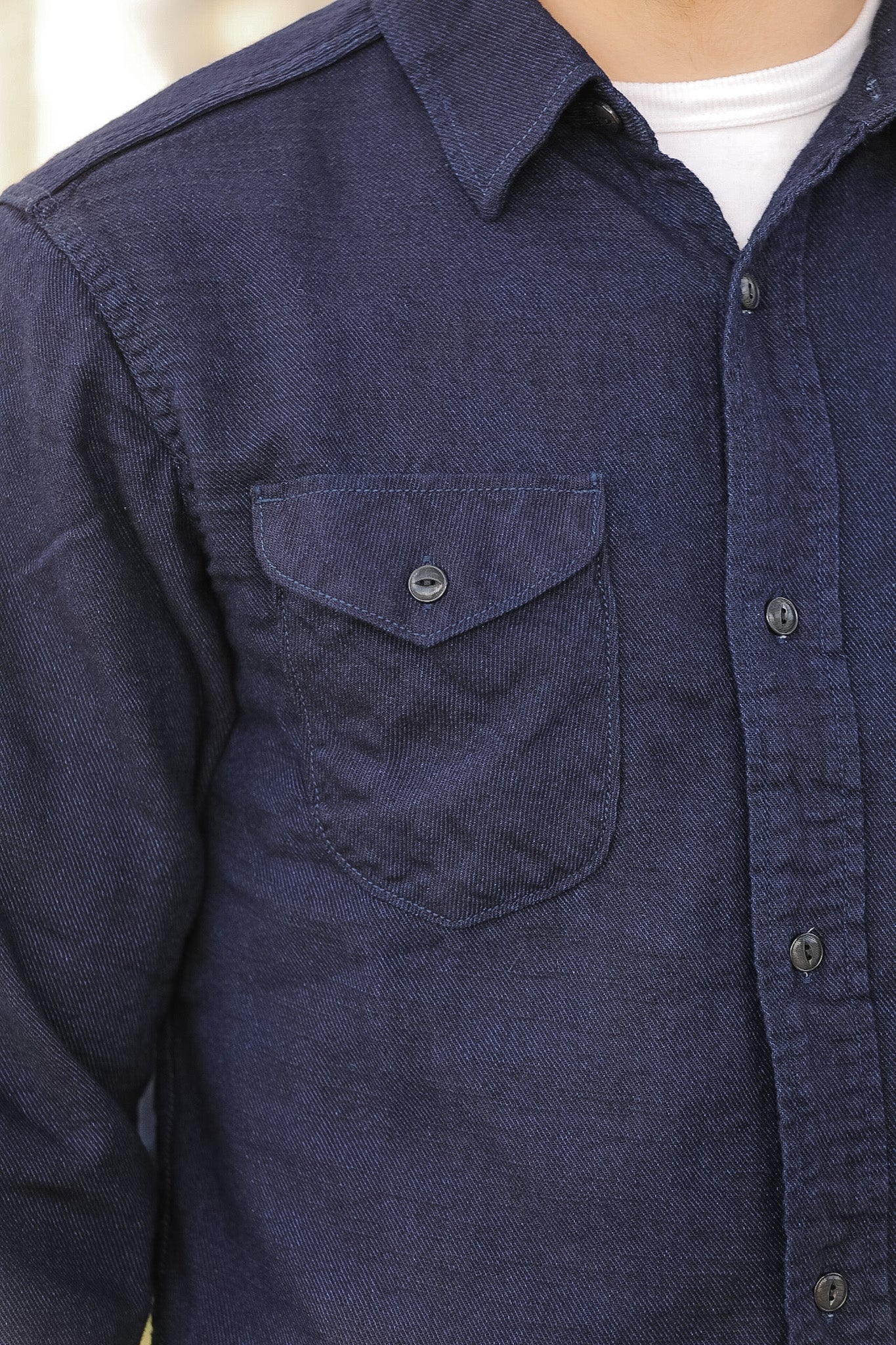 Navy blue shirt with a pocket and buttons on a neutral background