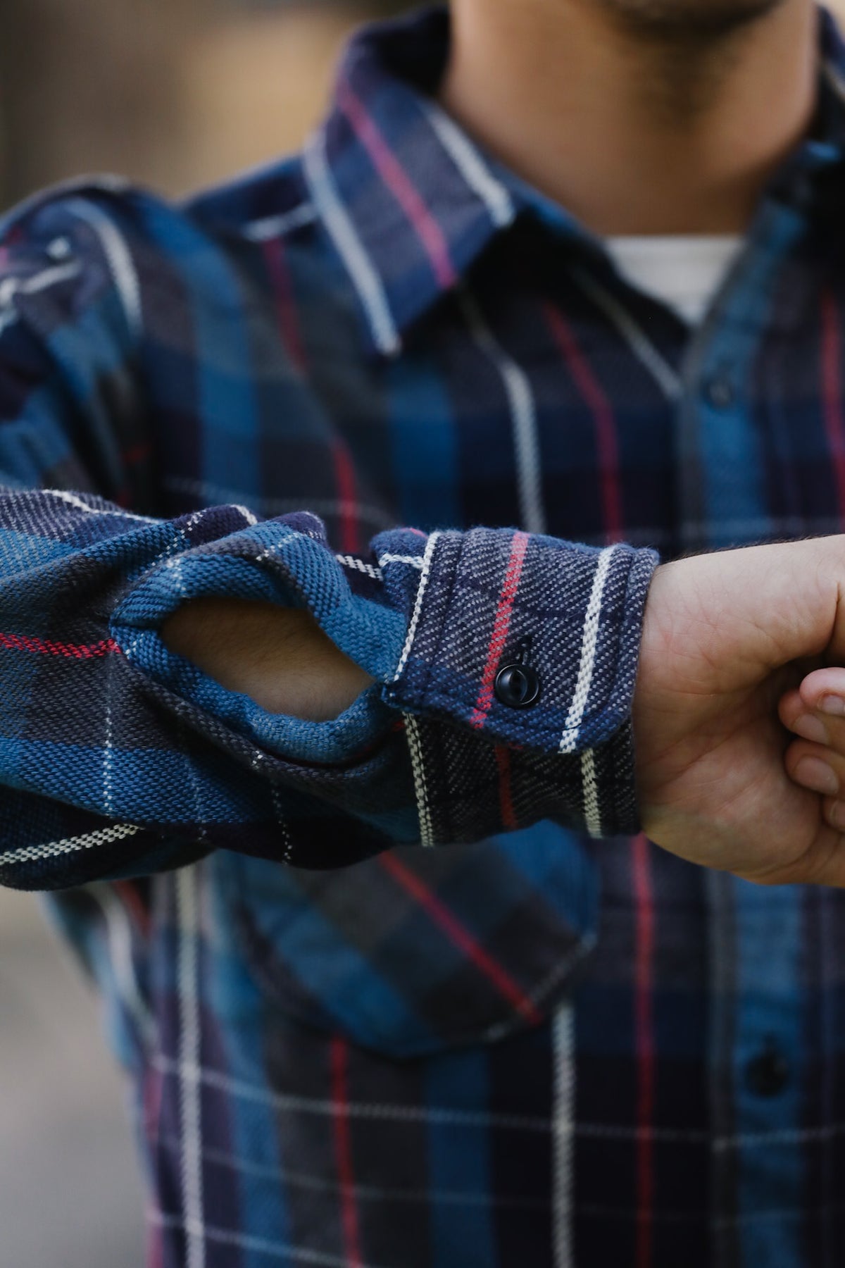 Close-up of a man wearing a blue plaid button-up shirt with rolled-up sleeves and a visible white undershirt.