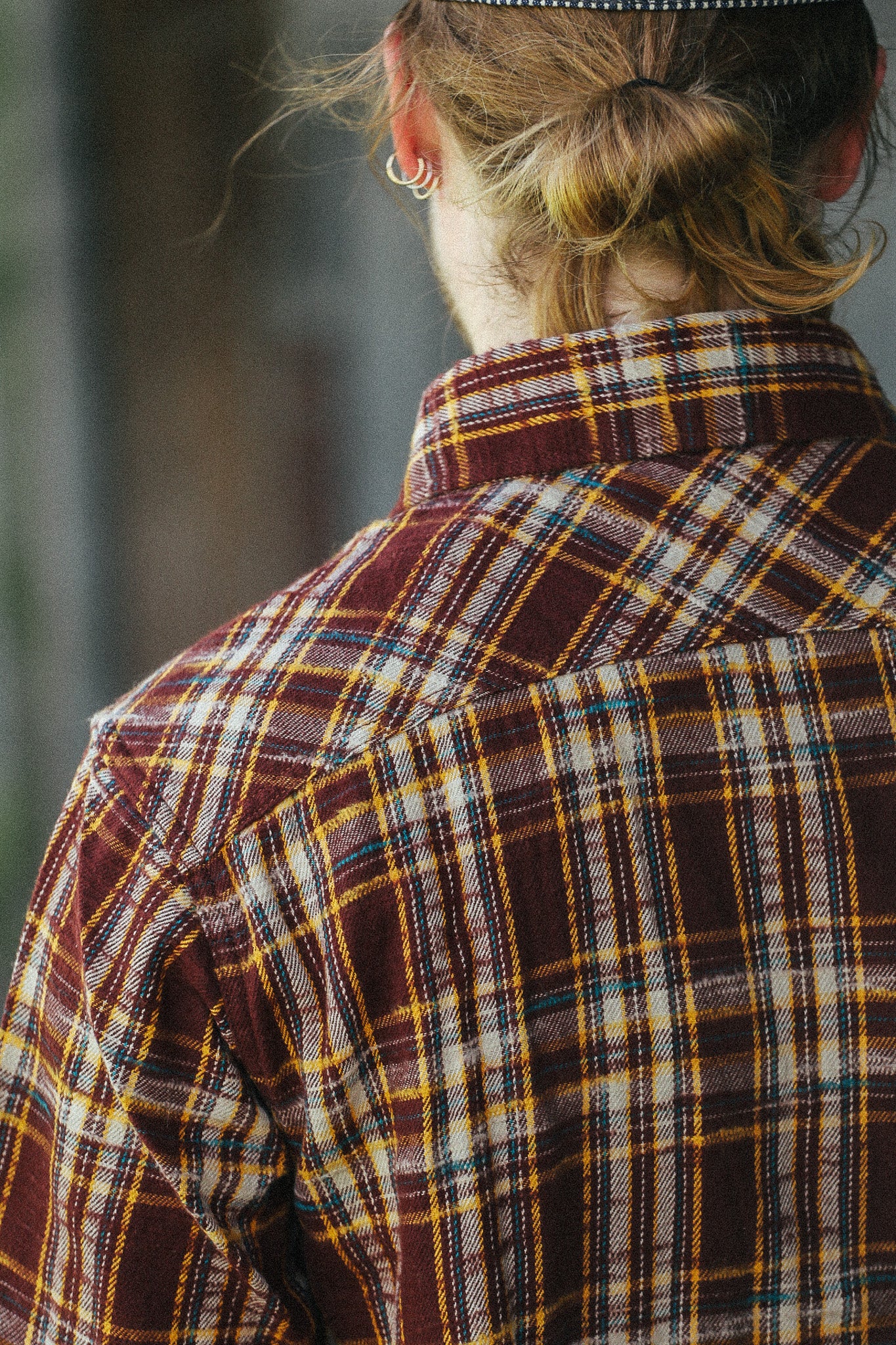 A close-up back view of a person wearing a brown, yellow, and white plaid flannel shirt.