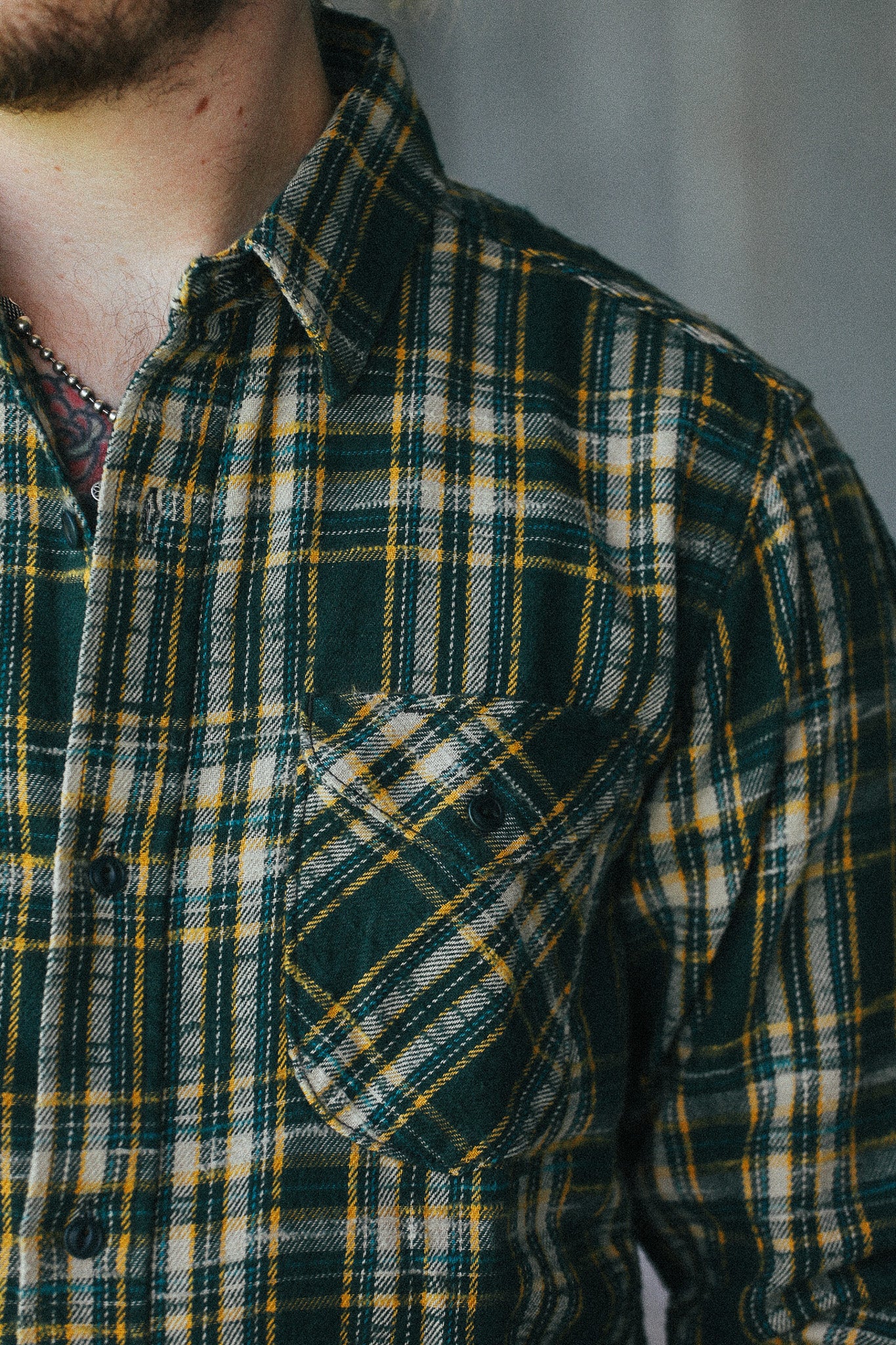 Close-up of a person wearing a dark green plaid flannel shirt with yellow and white stripes, featuring a chest pocket.